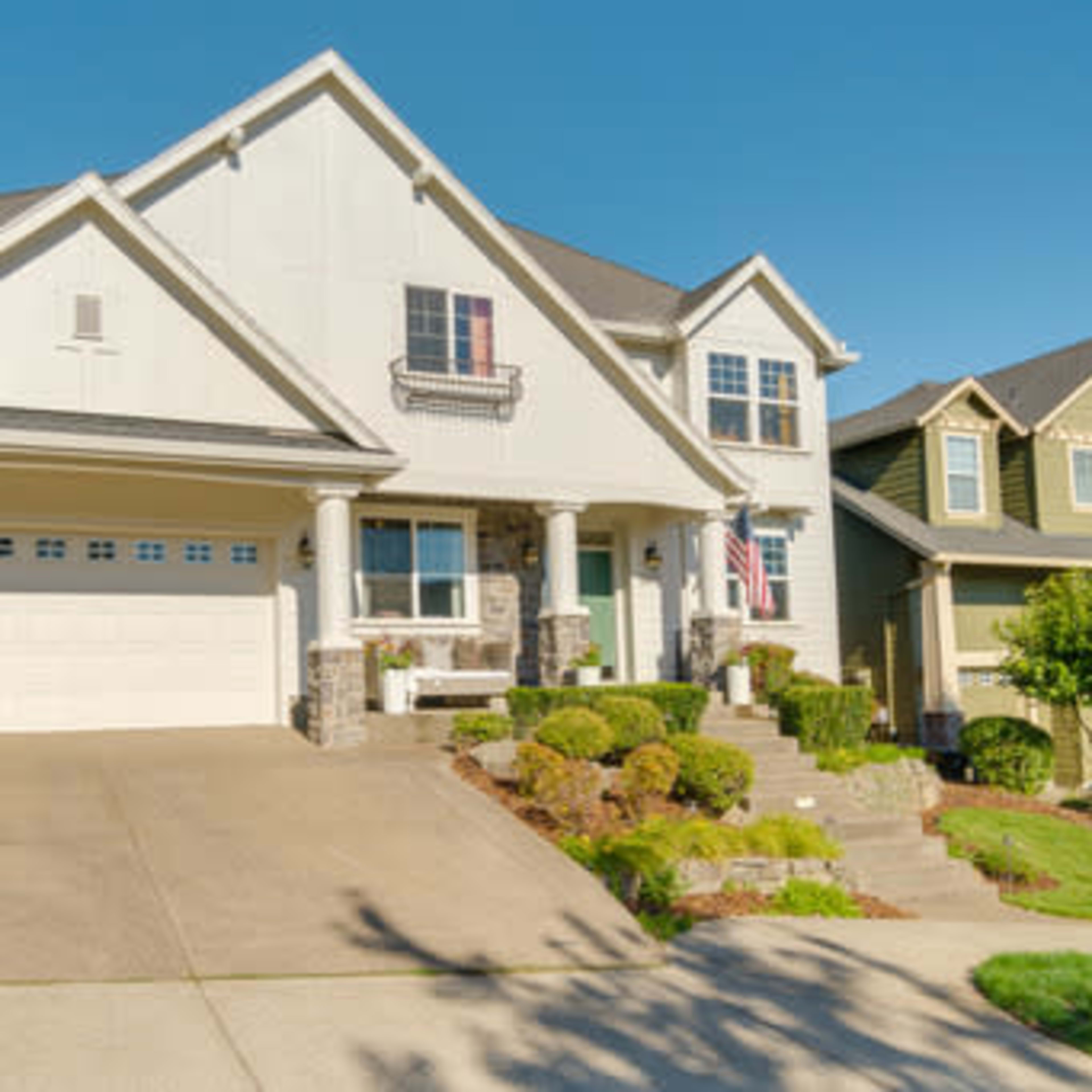A two-story house with a light-colored exterior, a neatly landscaped yard, and a driveway leading to a three-car garage.