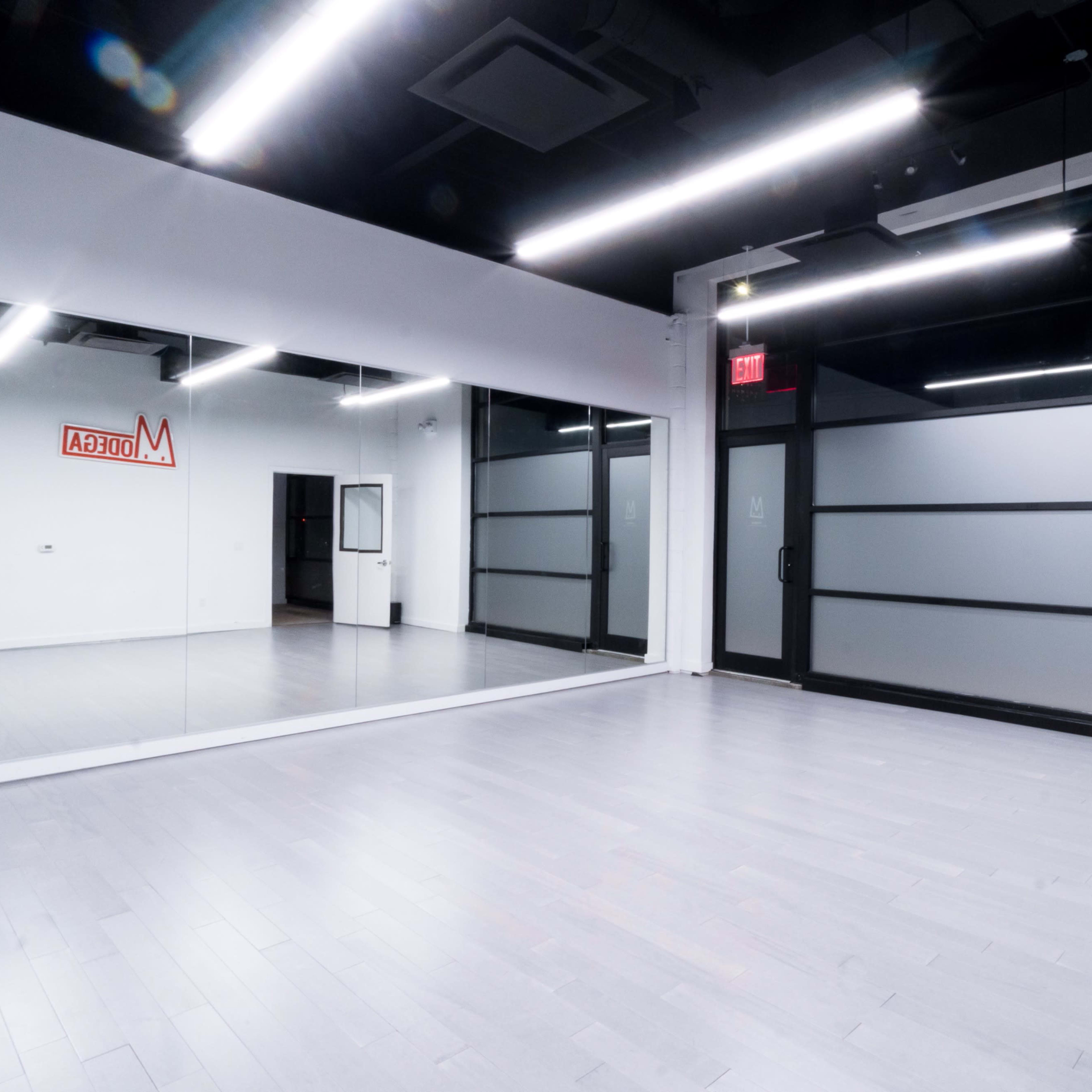 A spacious, minimalistic interior studio with large mirrors, gray flooring, and glass doors.