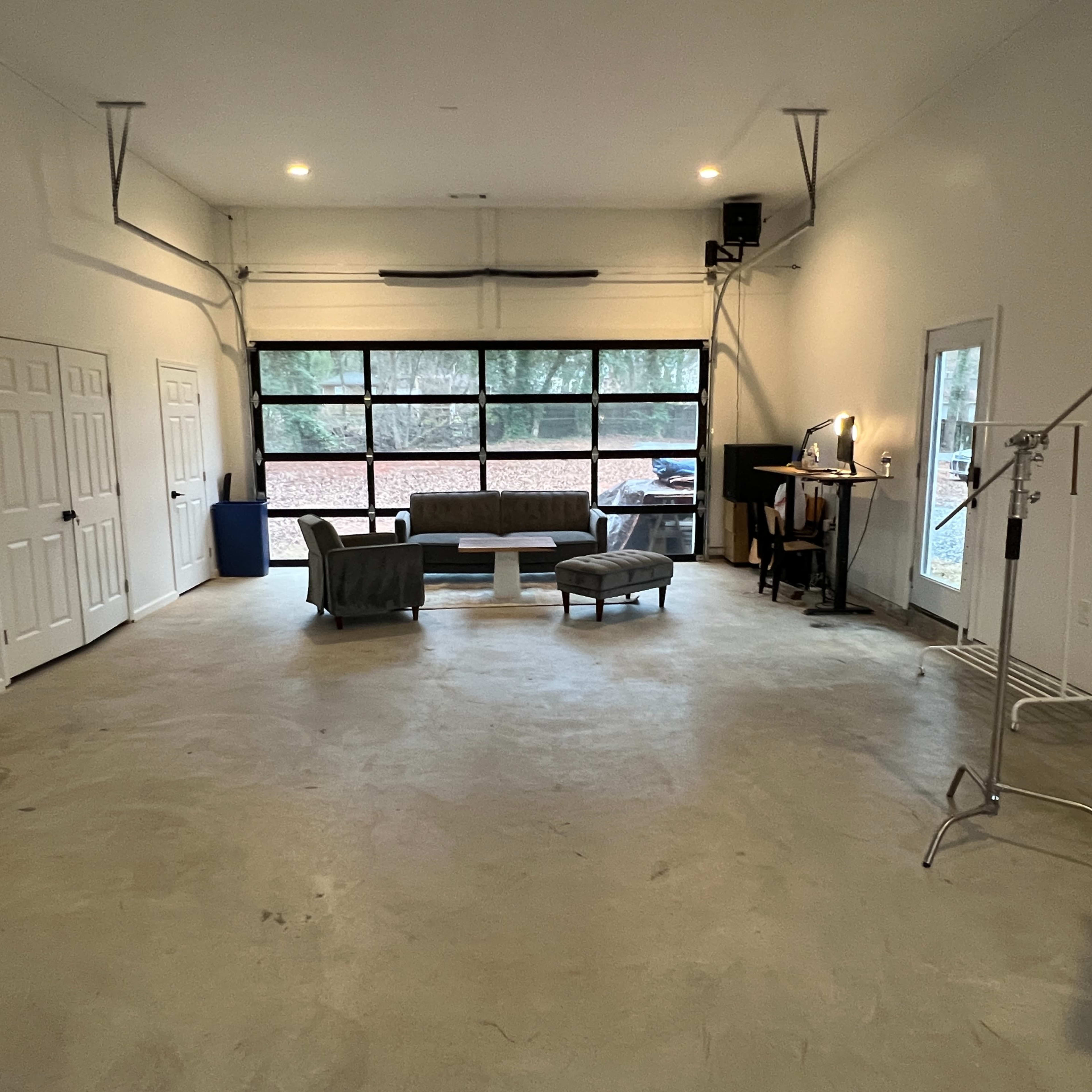 A spacious, empty room with a large garage door, a sofa, a coffee table, and various furniture against the walls.