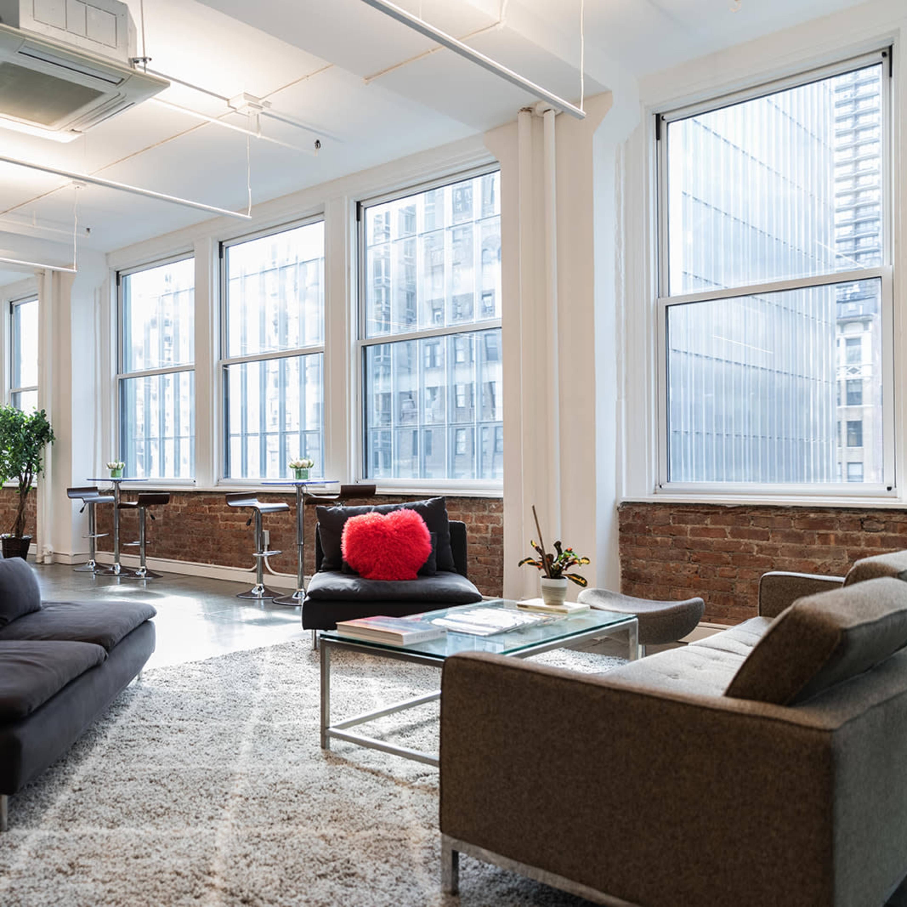 A modern, open-concept office space with large windows, multiple seating areas, and an area rug on the floor.