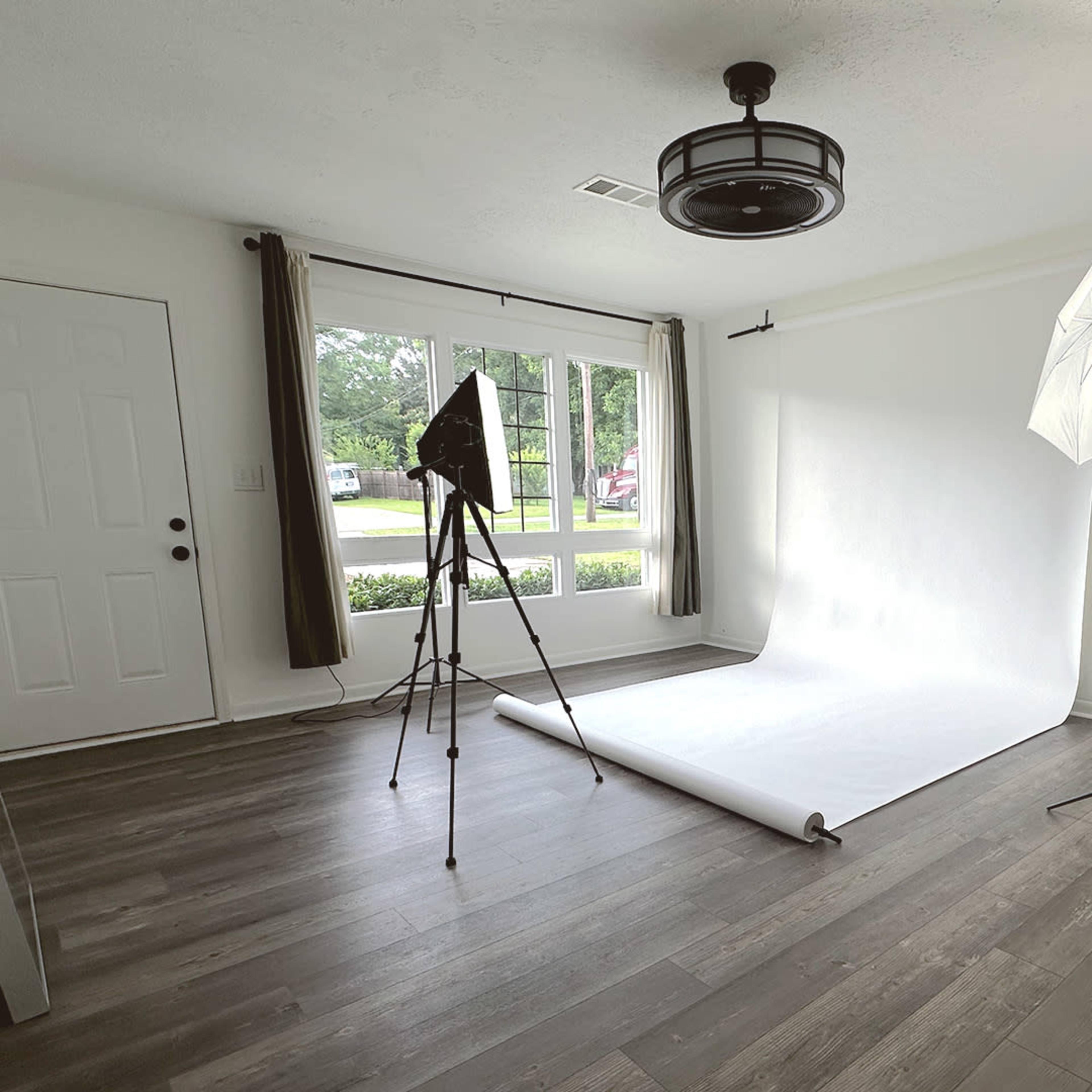 A photo studio setup features a white backdrop, two light sources, and a large window.