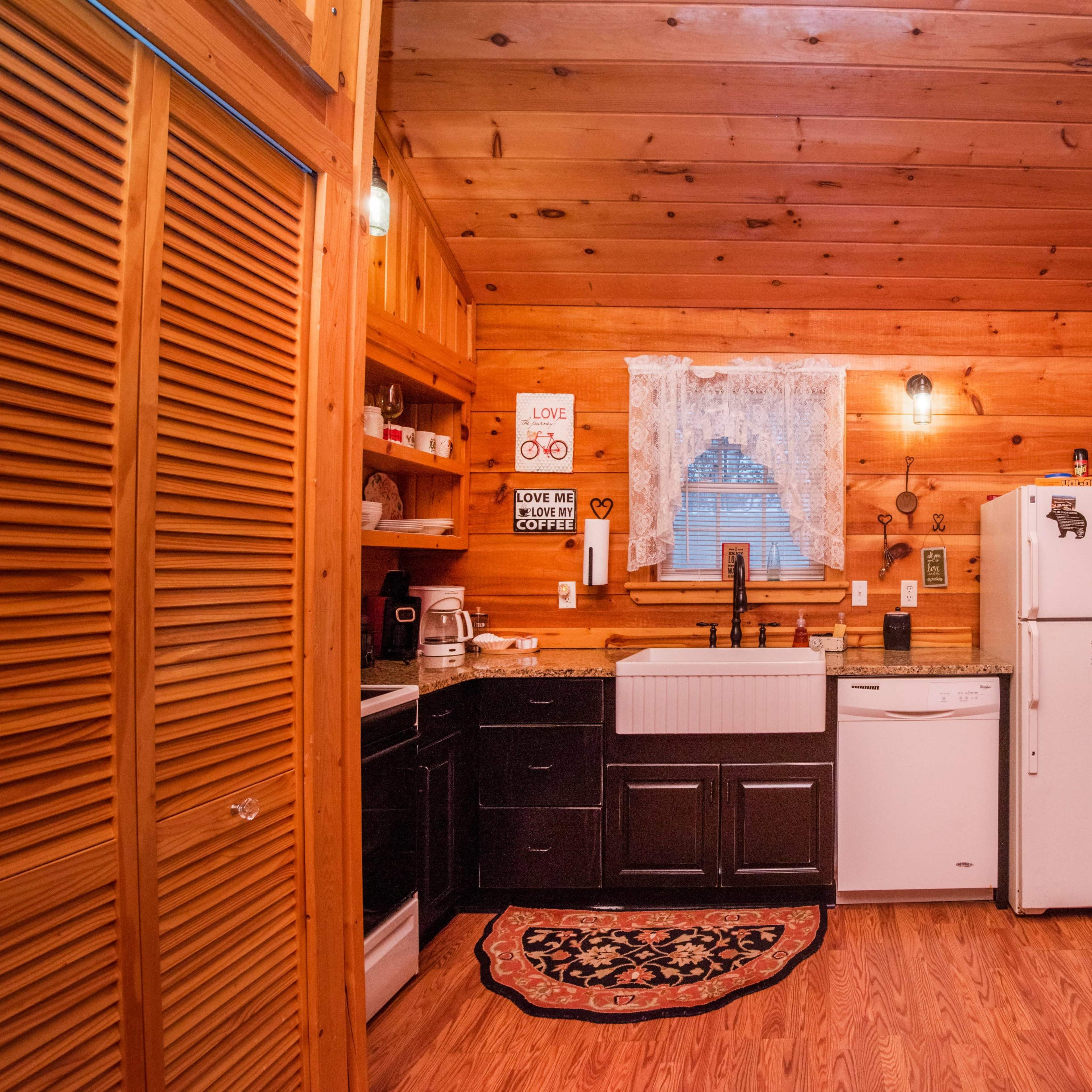 A wooden cabin kitchen featuring a sink, refrigerator, and various kitchen appliances against a backdrop of wood-paneled walls.