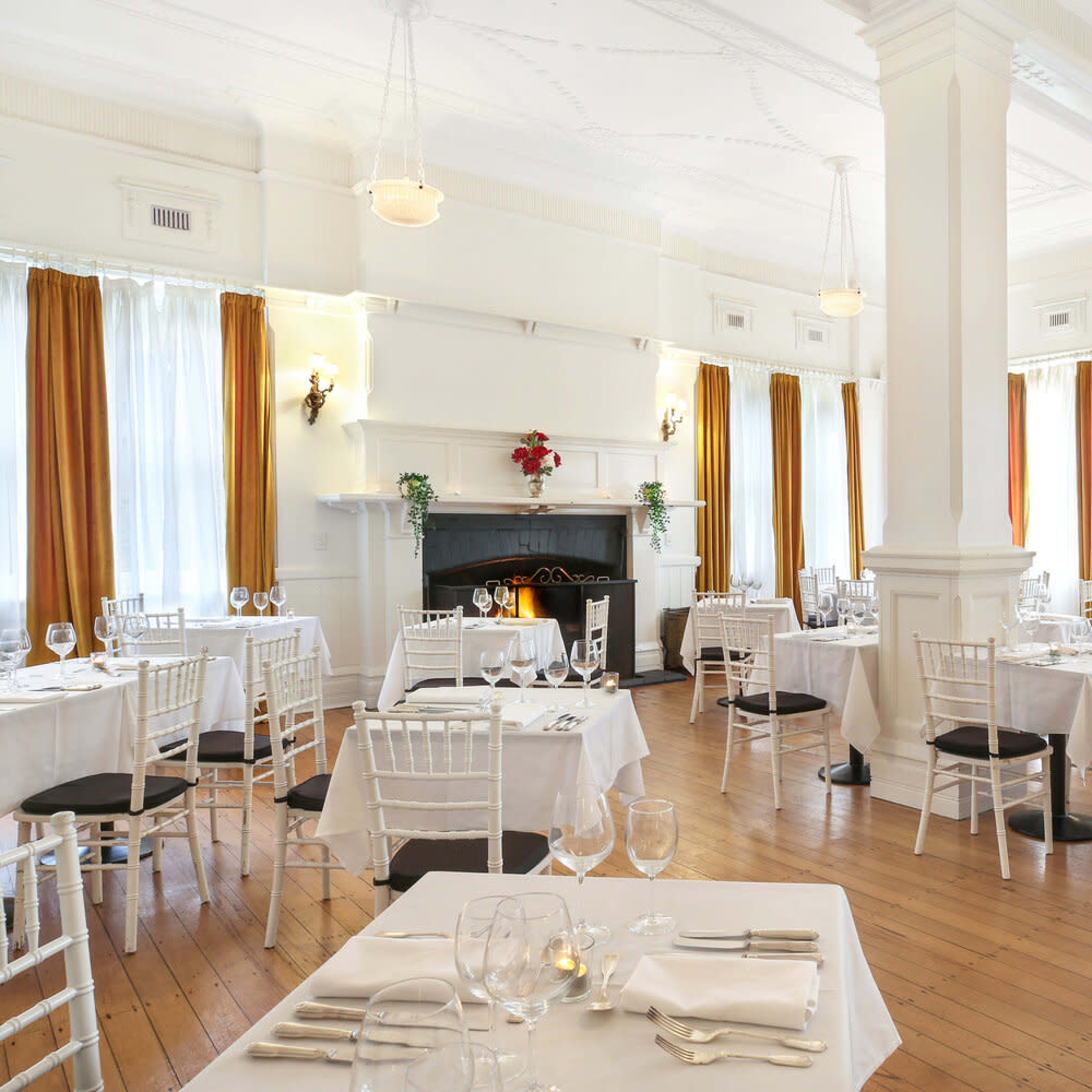 A well-lit restaurant featuring neatly arranged tables with white tablecloths, surrounded by large windows adorned with orange curtains.