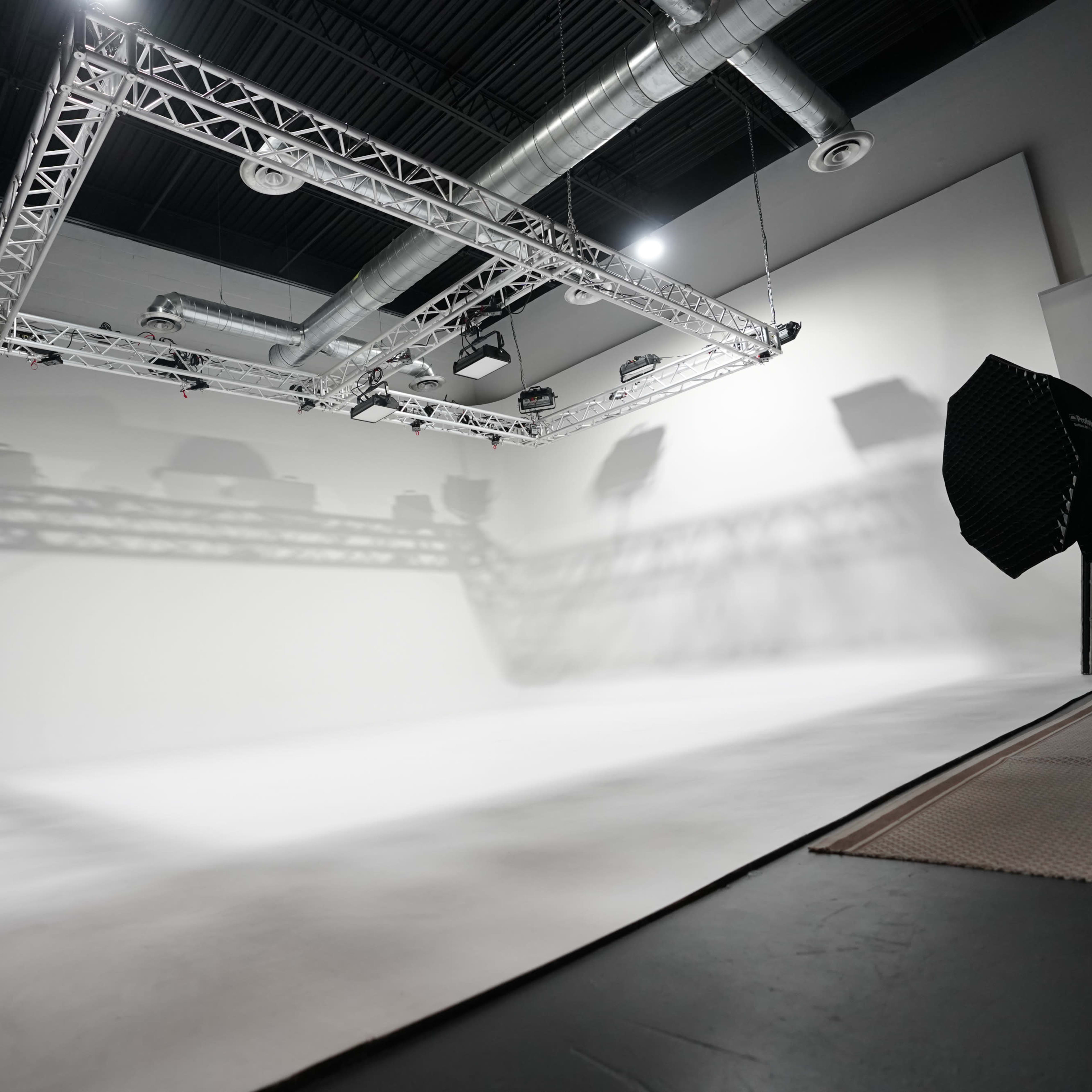 A spacious, well-lit photography studio with a white backdrop and overhead lighting equipment.