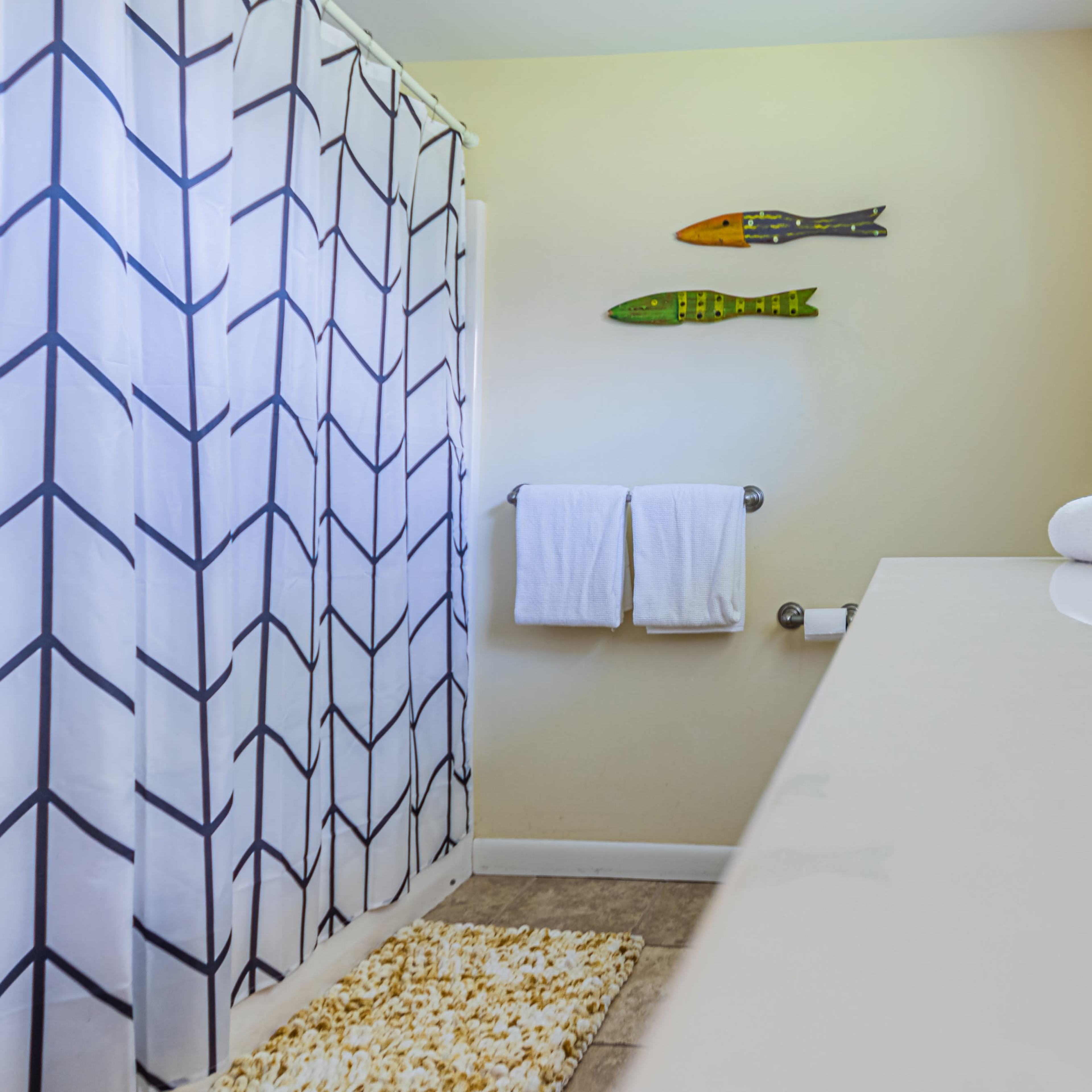 A bright bathroom with a shower curtain featuring a geometric pattern, two towels hanging on a bar, and a small plant on the countertop.
