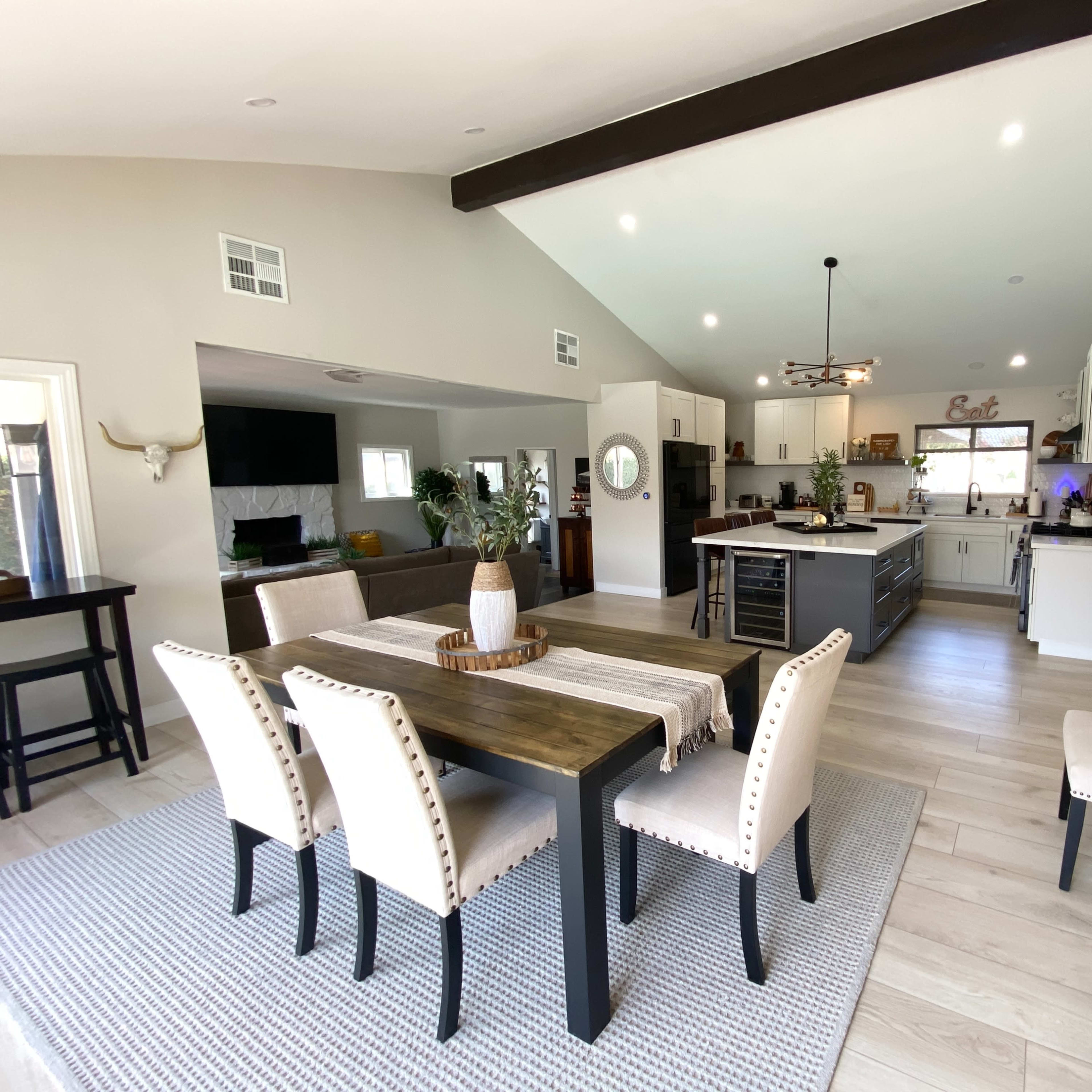 A modern, open-concept kitchen and dining area featuring a wooden dining table, beige upholstered chairs, and a kitchen island with bar seating.