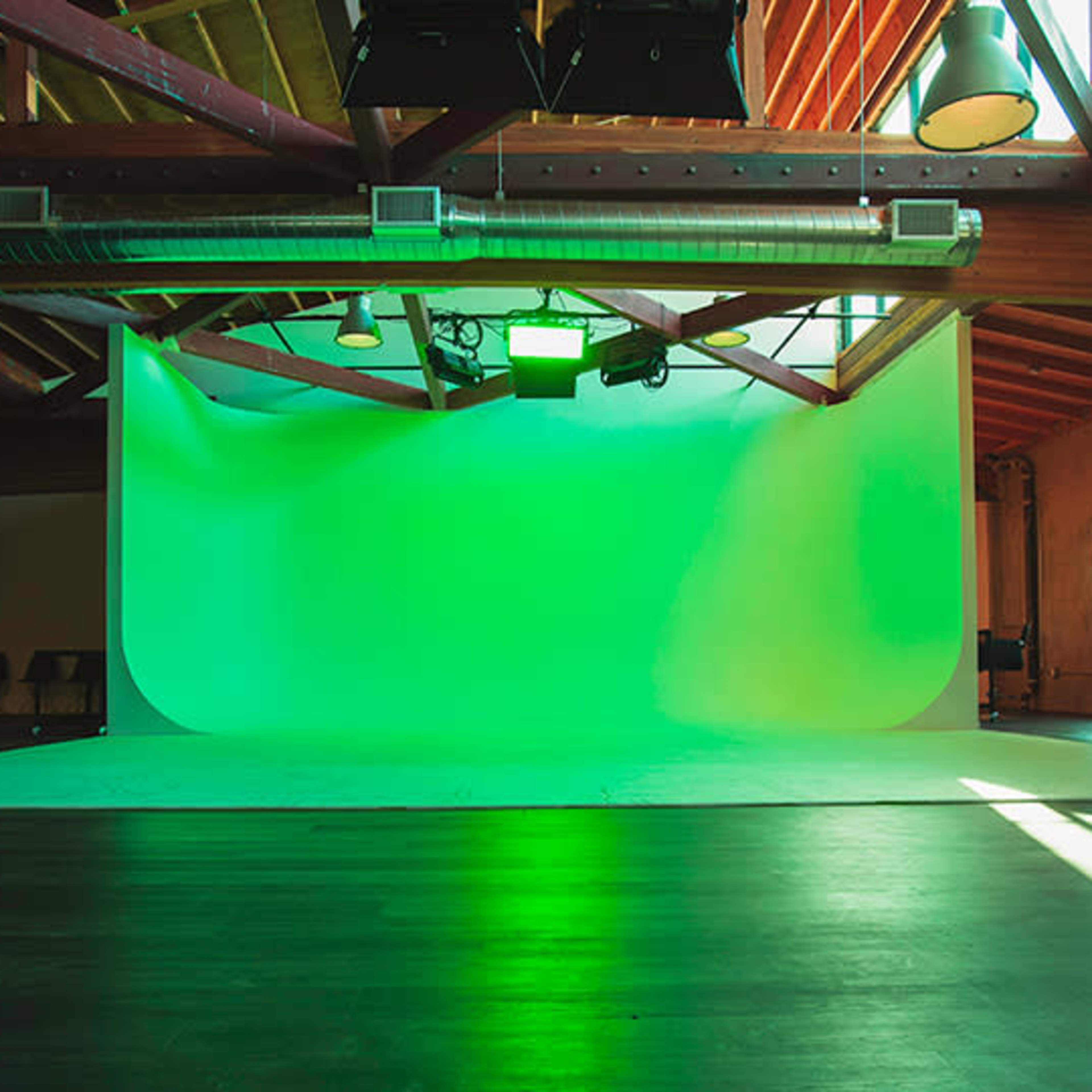 An empty studio space features a large green backdrop with bright lighting and wooden ceilings.