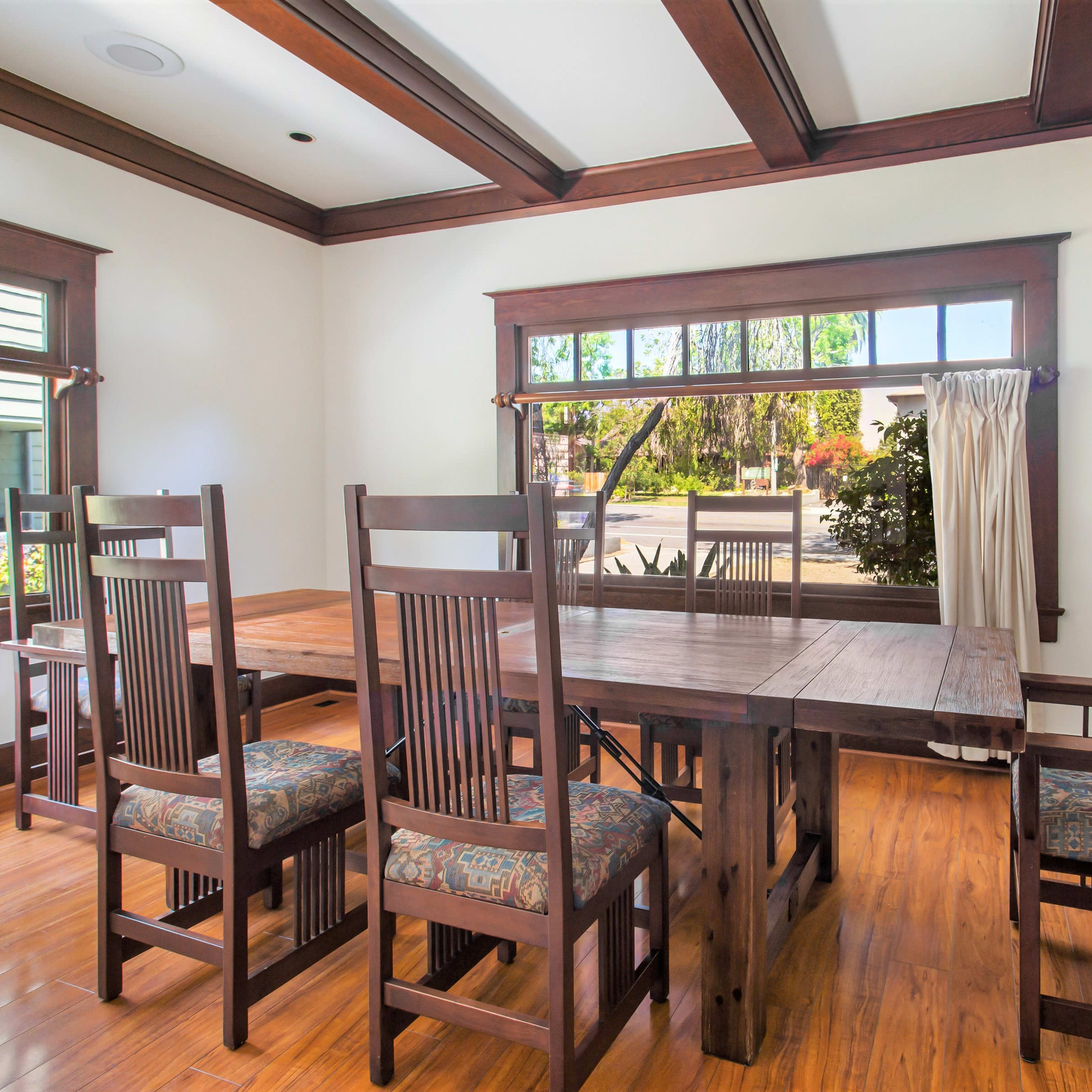 A spacious dining room features a wooden table surrounded by six chairs, with large windows allowing natural light to enter.