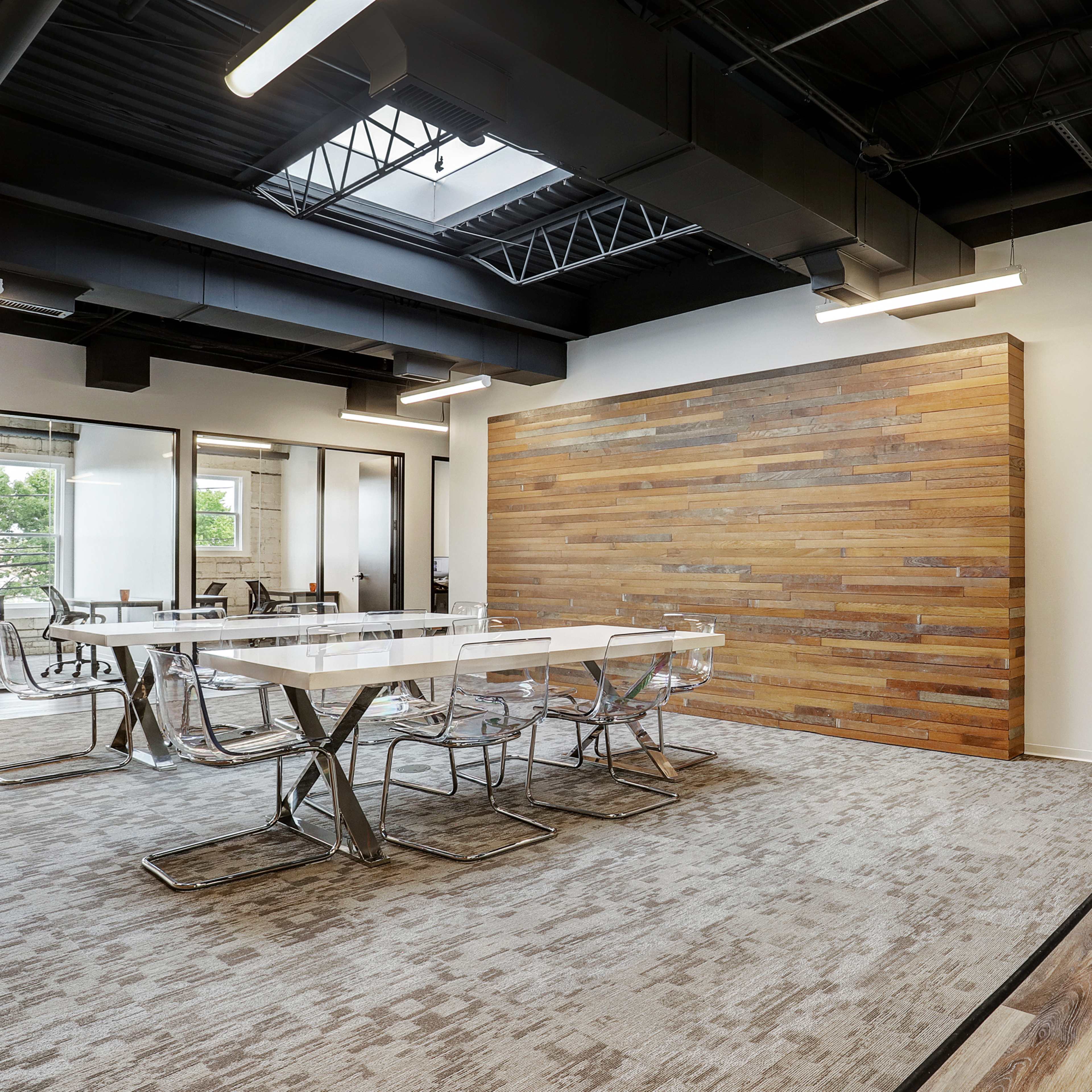 A modern office interior featuring a wooden accent wall, a glass conference table with metal chairs, and a layout that includes open spaces and glass-walled meeting rooms.