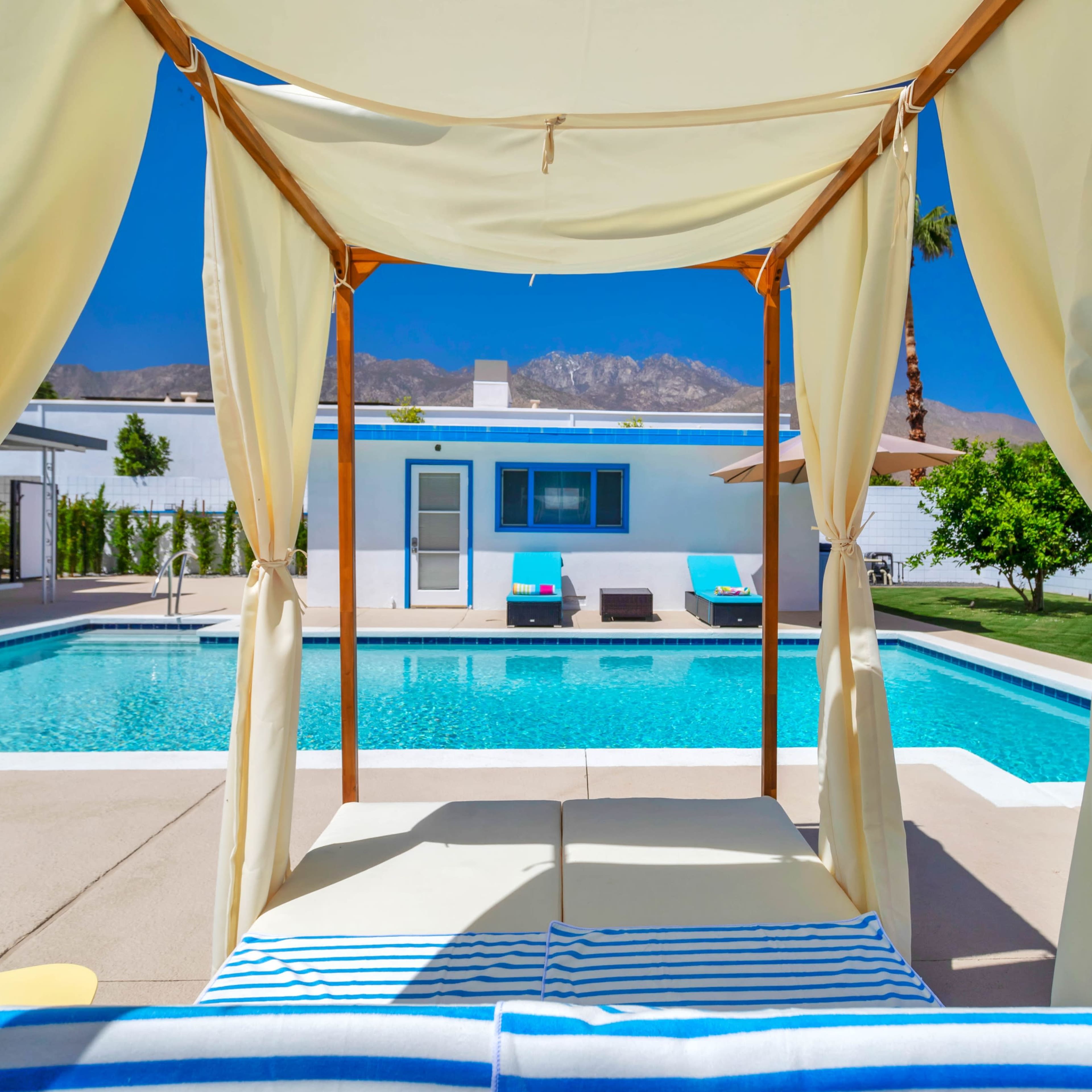A pool area with a cabana overlooking a turquoise swimming pool surrounded by lounge chairs and a backdrop of mountains.