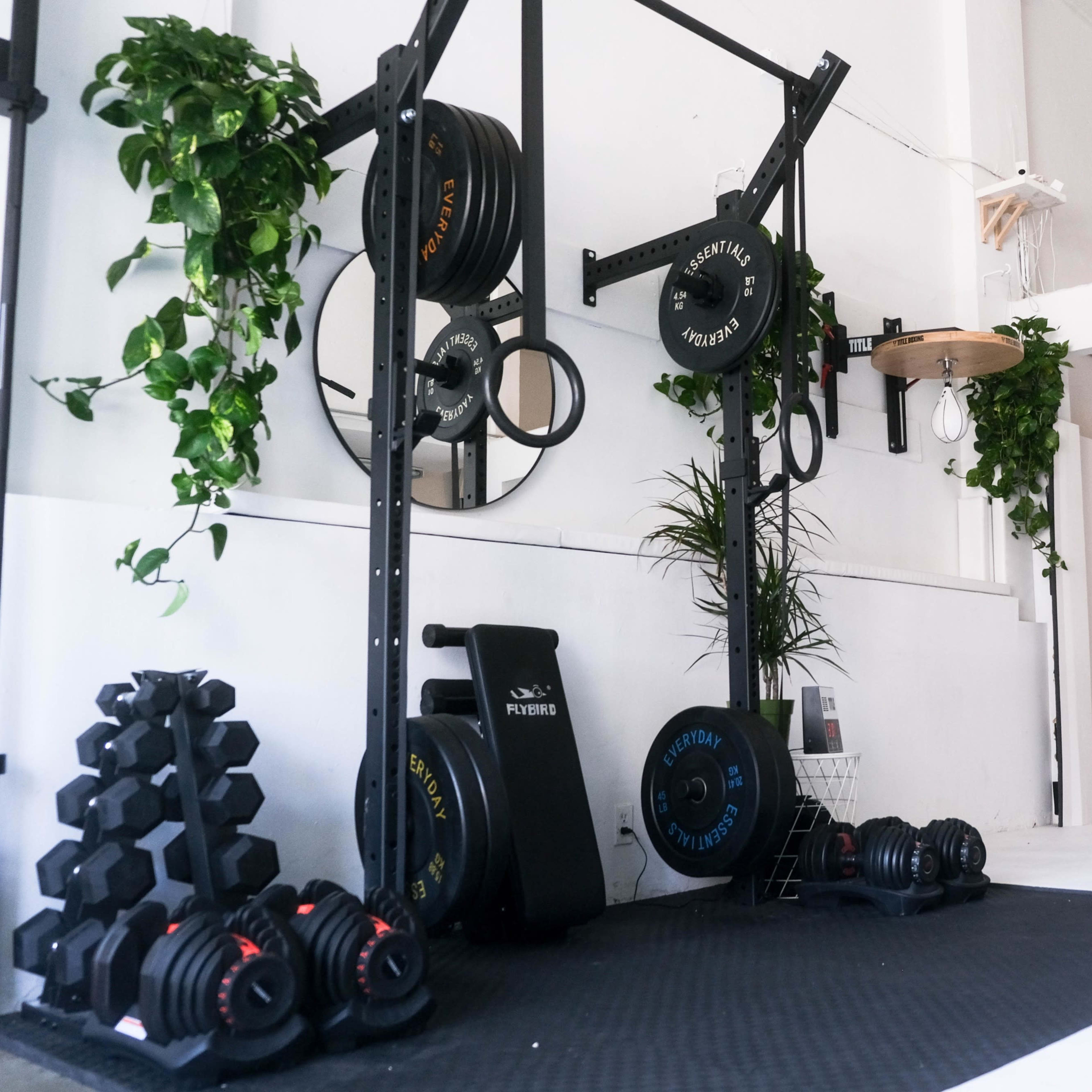 A minimalist gym space with a set of free weights, a barbell rack, and a heavy bag suspended from the ceiling.