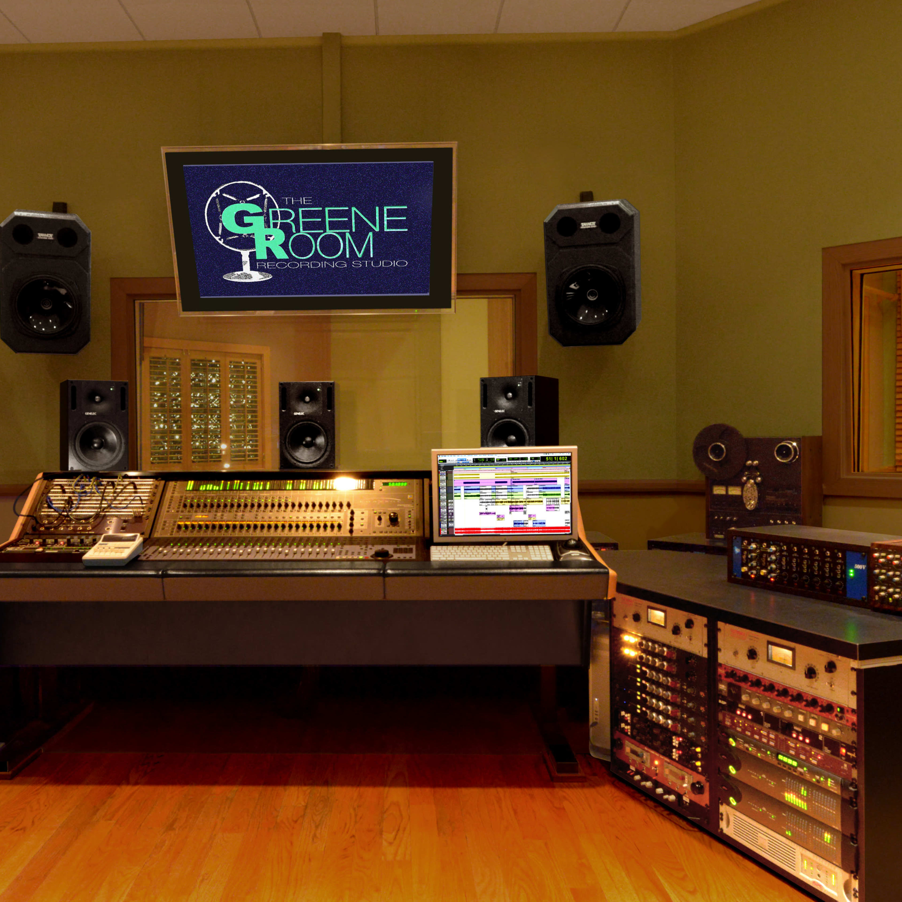 A recording studio with a central mixing console, a computer displaying audio software, and multiple speakers and racks of audio equipment.