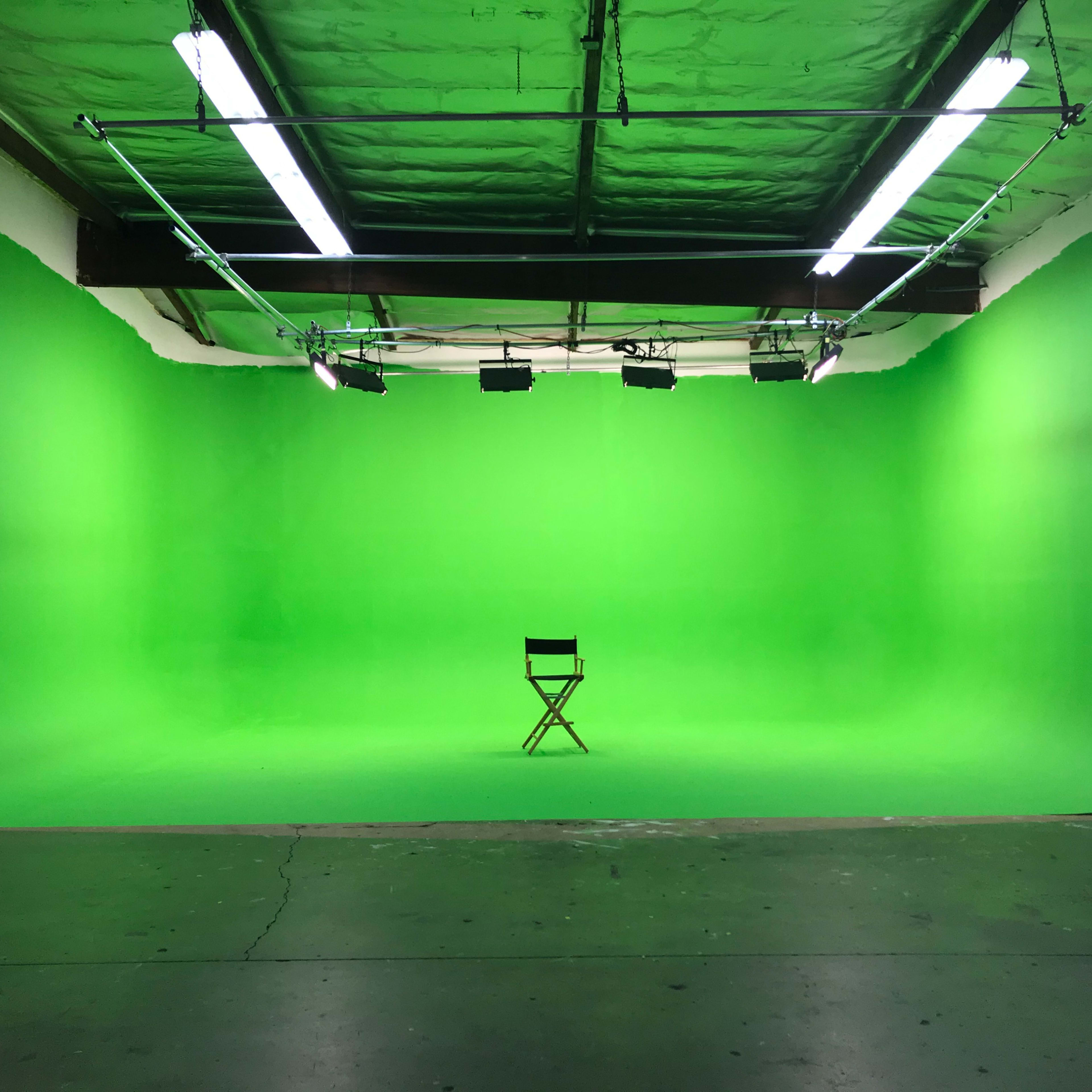 A green screen studio features a single director's chair centered in an empty space.