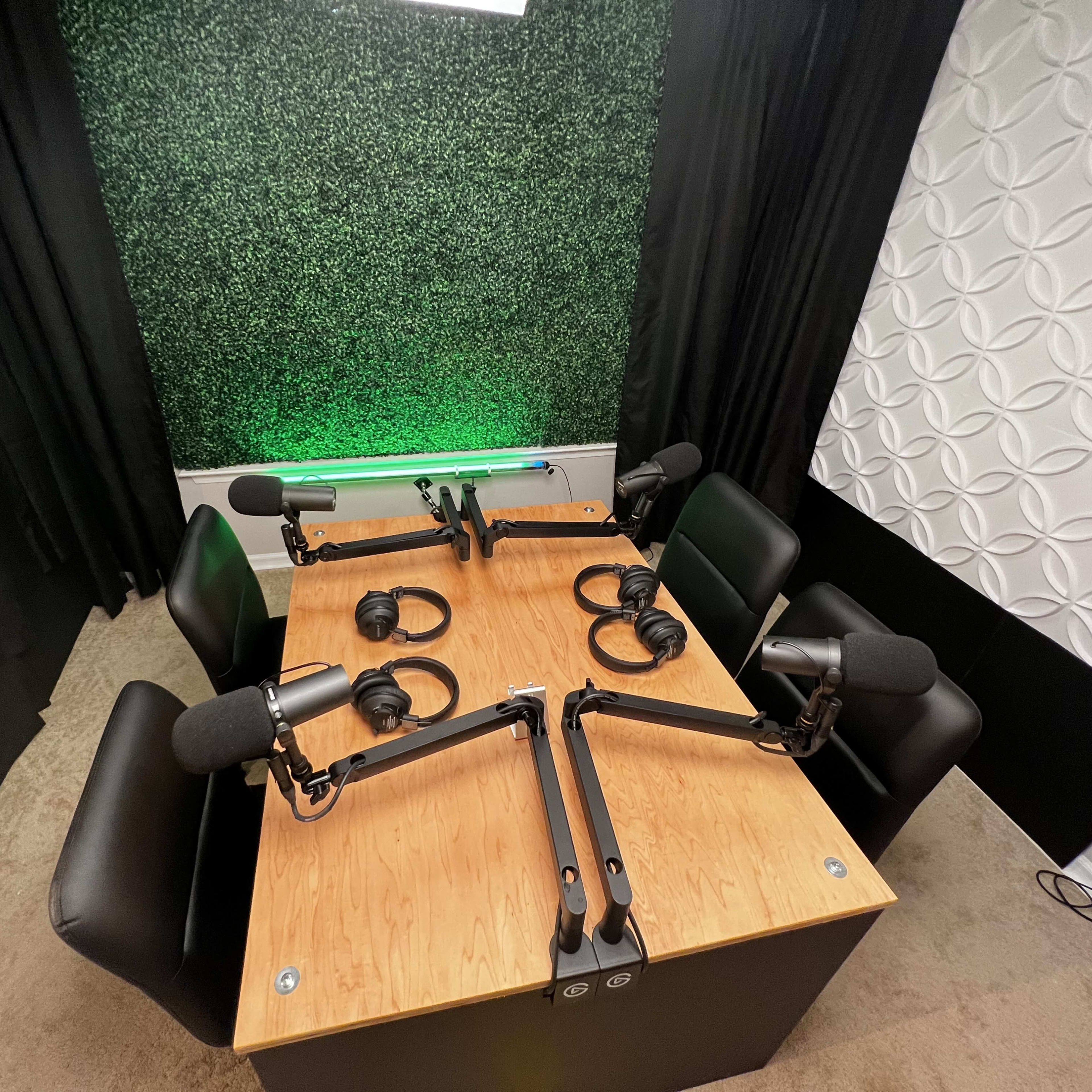 A podcast studio featuring a wooden table with four chairs, two microphone arms, and headphones arranged for recording.