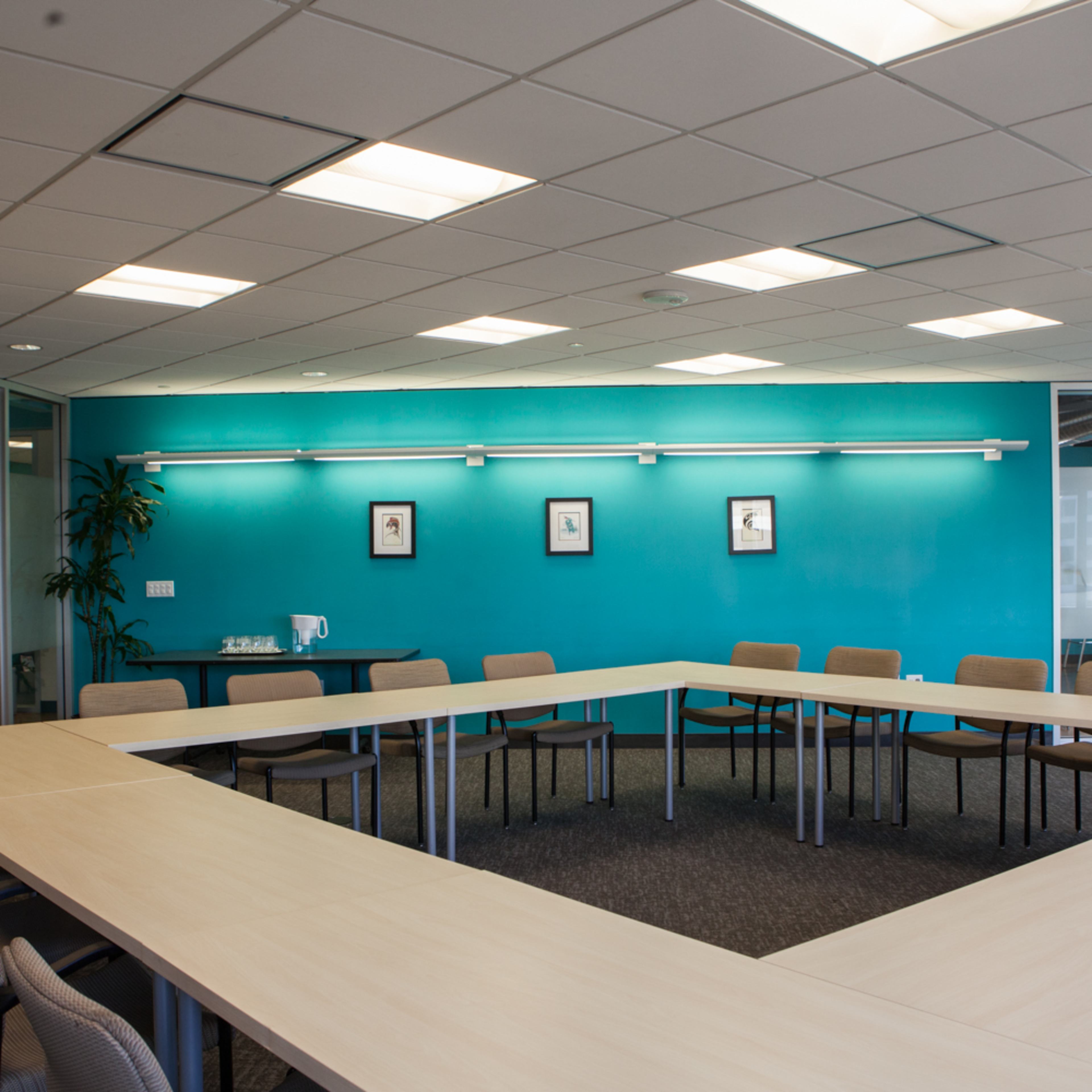 A conference room featuring a large, U-shaped table surrounded by chairs, with blue walls and a glass-walled meeting area.