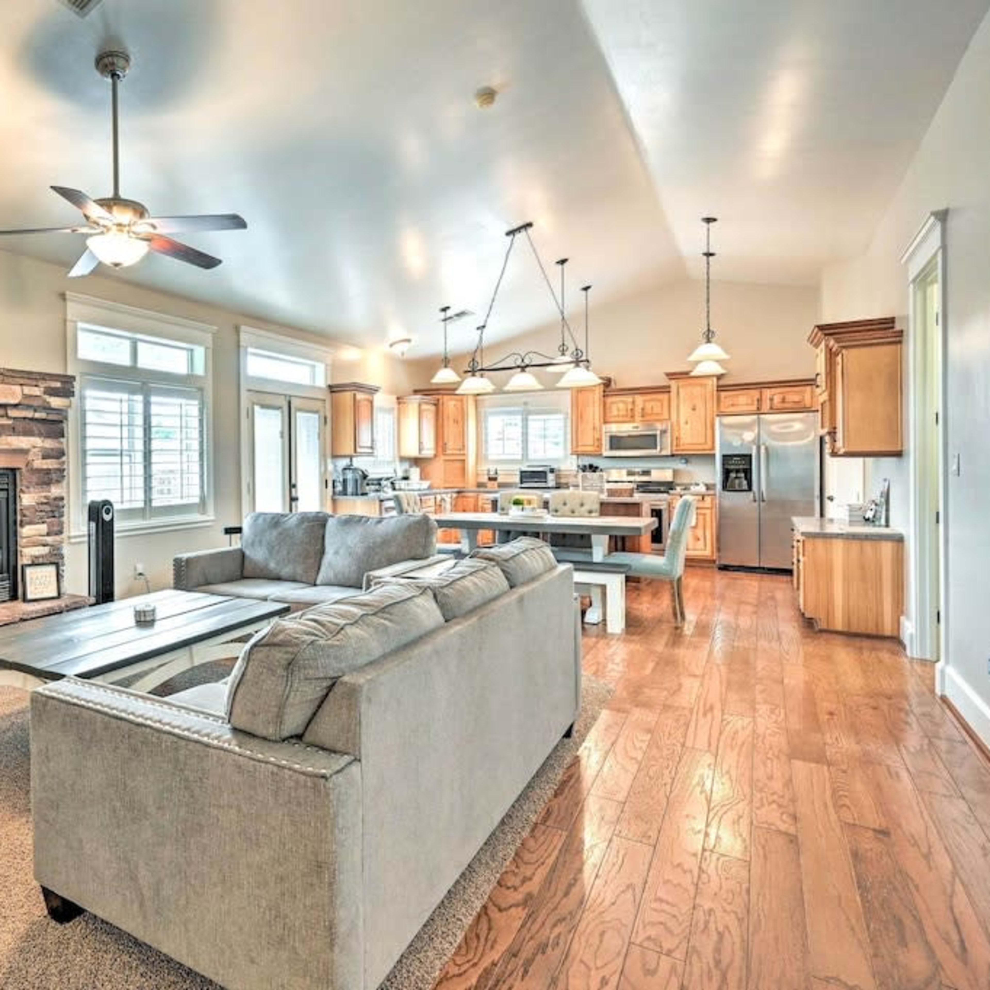 A spacious, open-concept living area with a comfortable sofa, a dining table, and a kitchen featuring wooden cabinets and a stone fireplace.