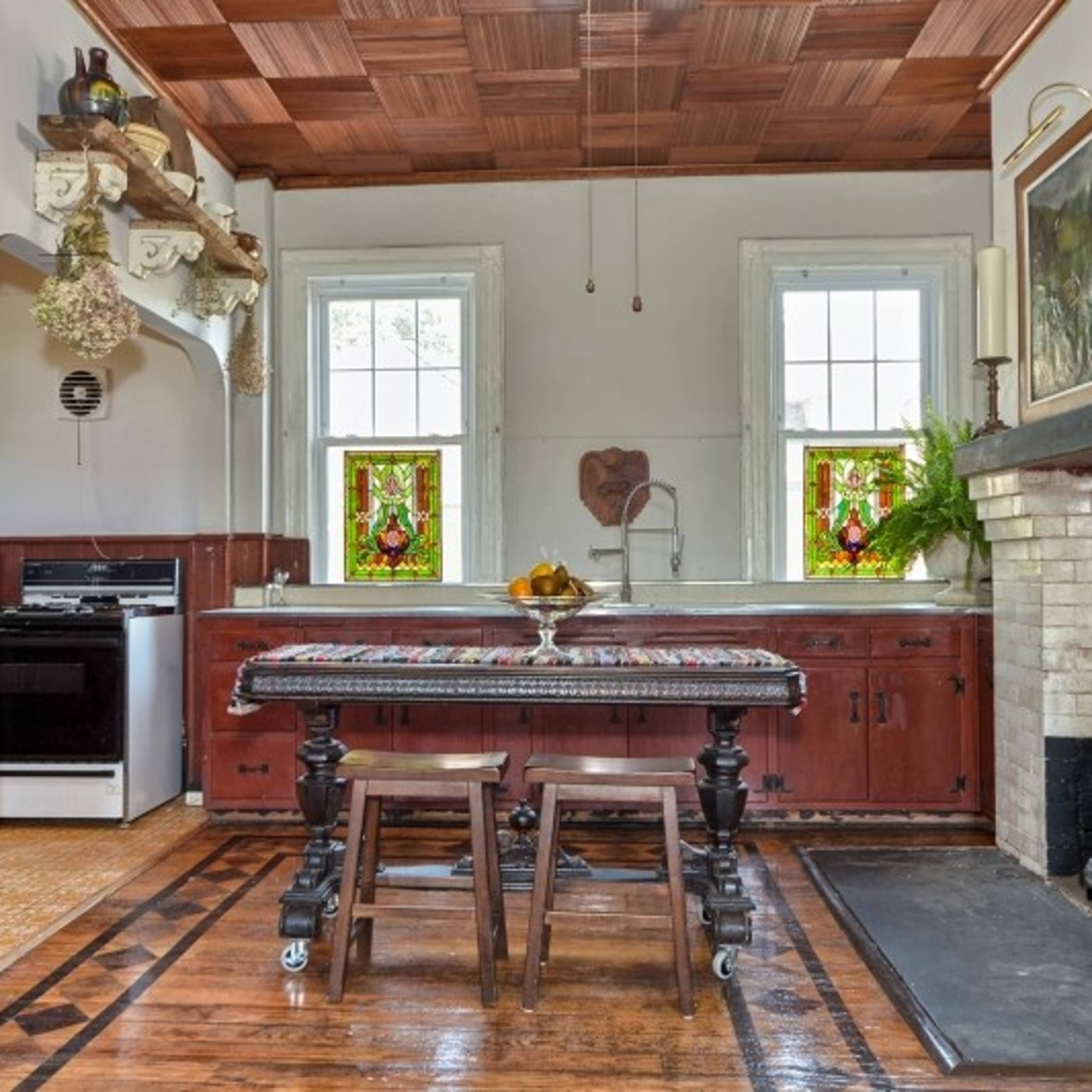 A rustic kitchen featuring a wooden table, vintage cabinets, and stained glass windows with a red and green design.