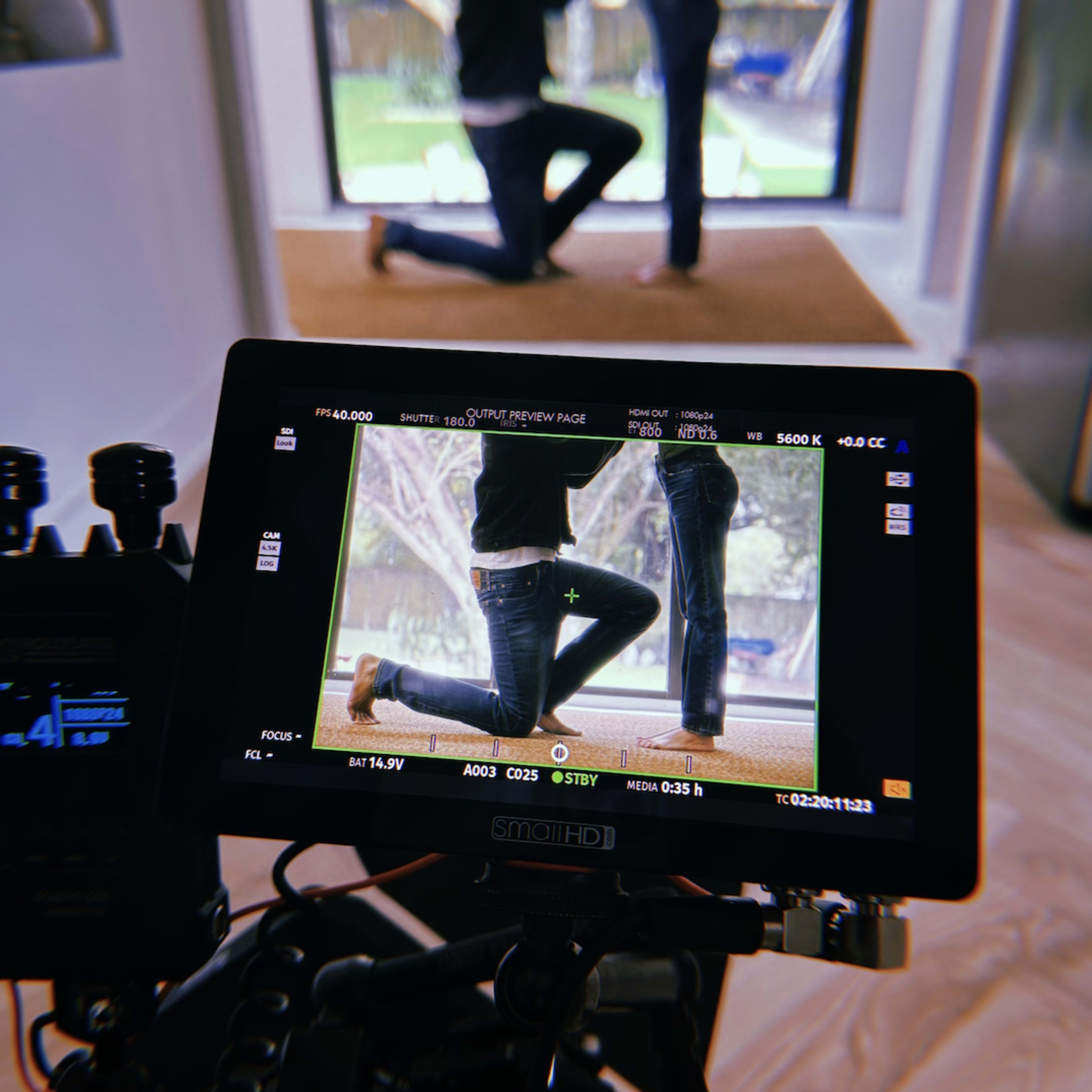 A camera monitor displays a couple kneeling in front of a large glass door while a photographer captures the moment.
