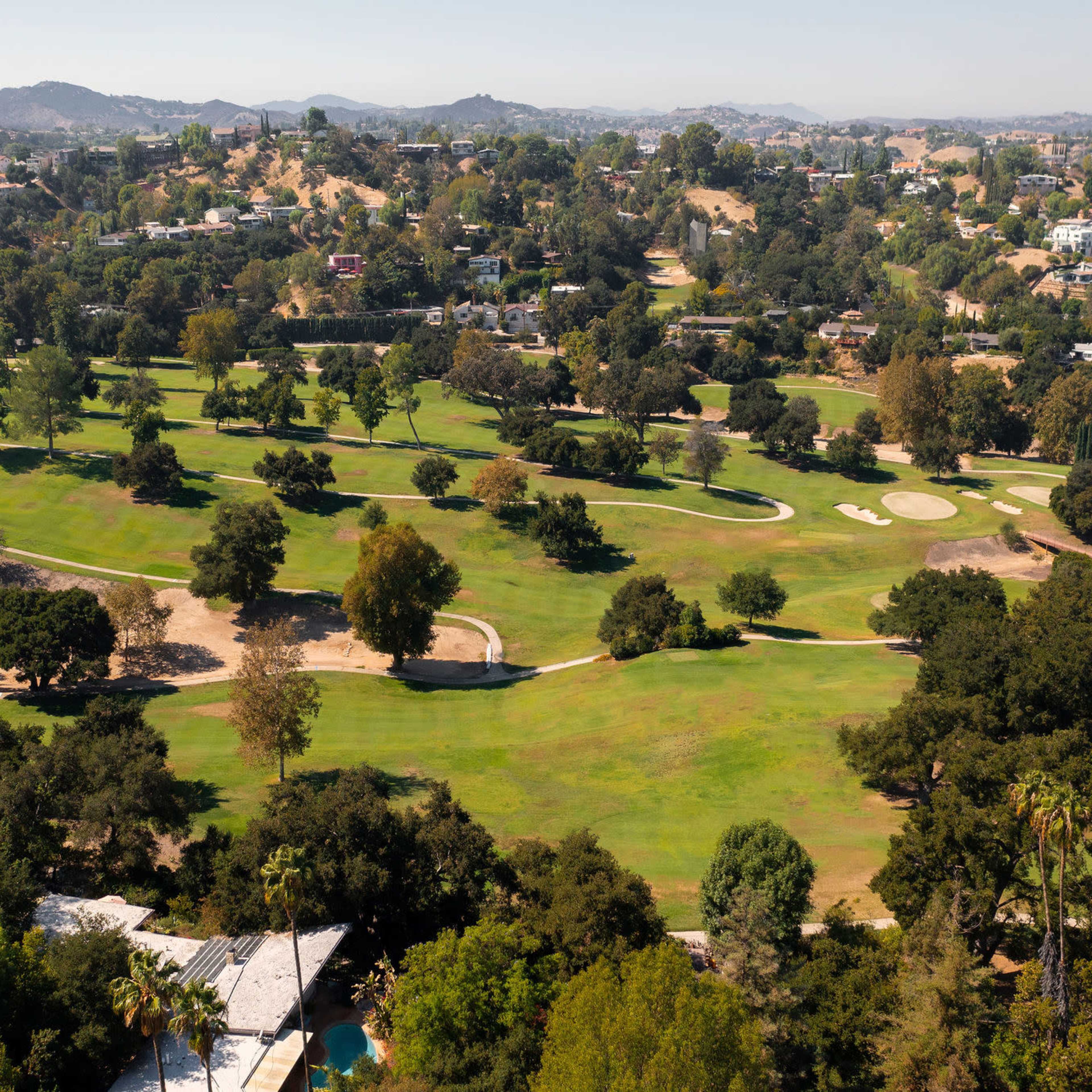 An aerial view of a green golf course surrounded by hills and residential areas.