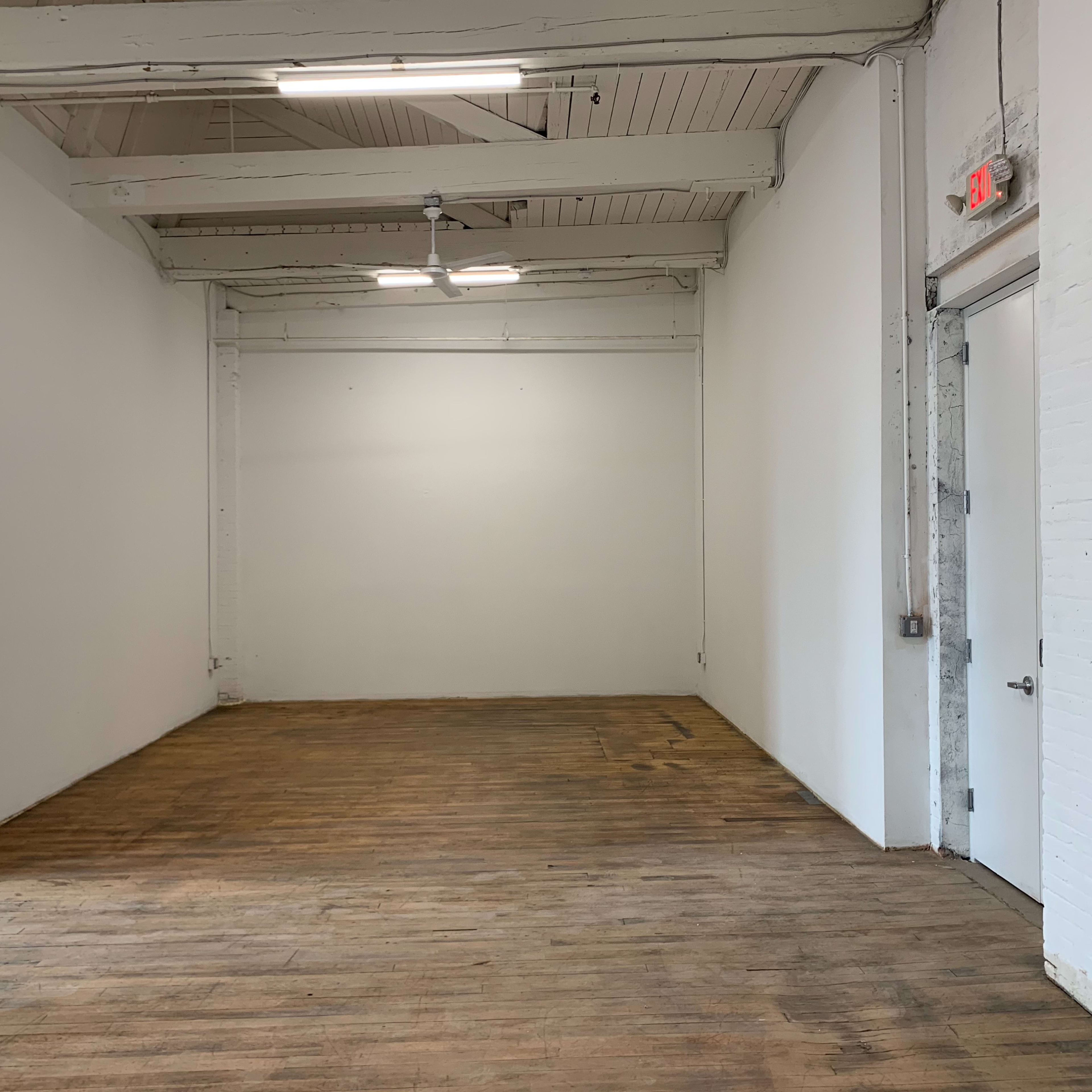 A sparsely furnished, empty room with wooden floors and white walls.