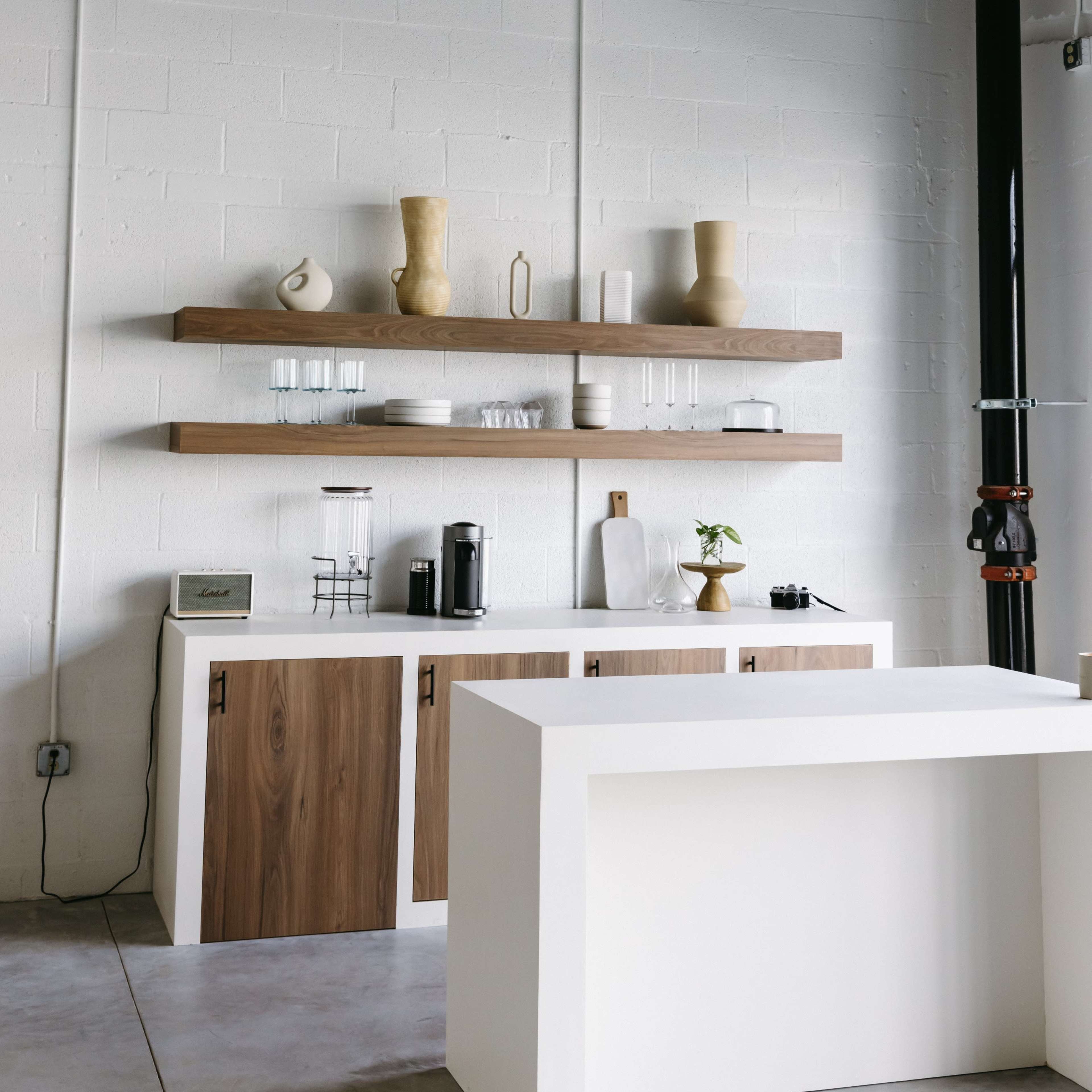 A minimalist kitchen features wooden shelves with decorative vases and glassware, above a counter area with a coffee maker and small plant.