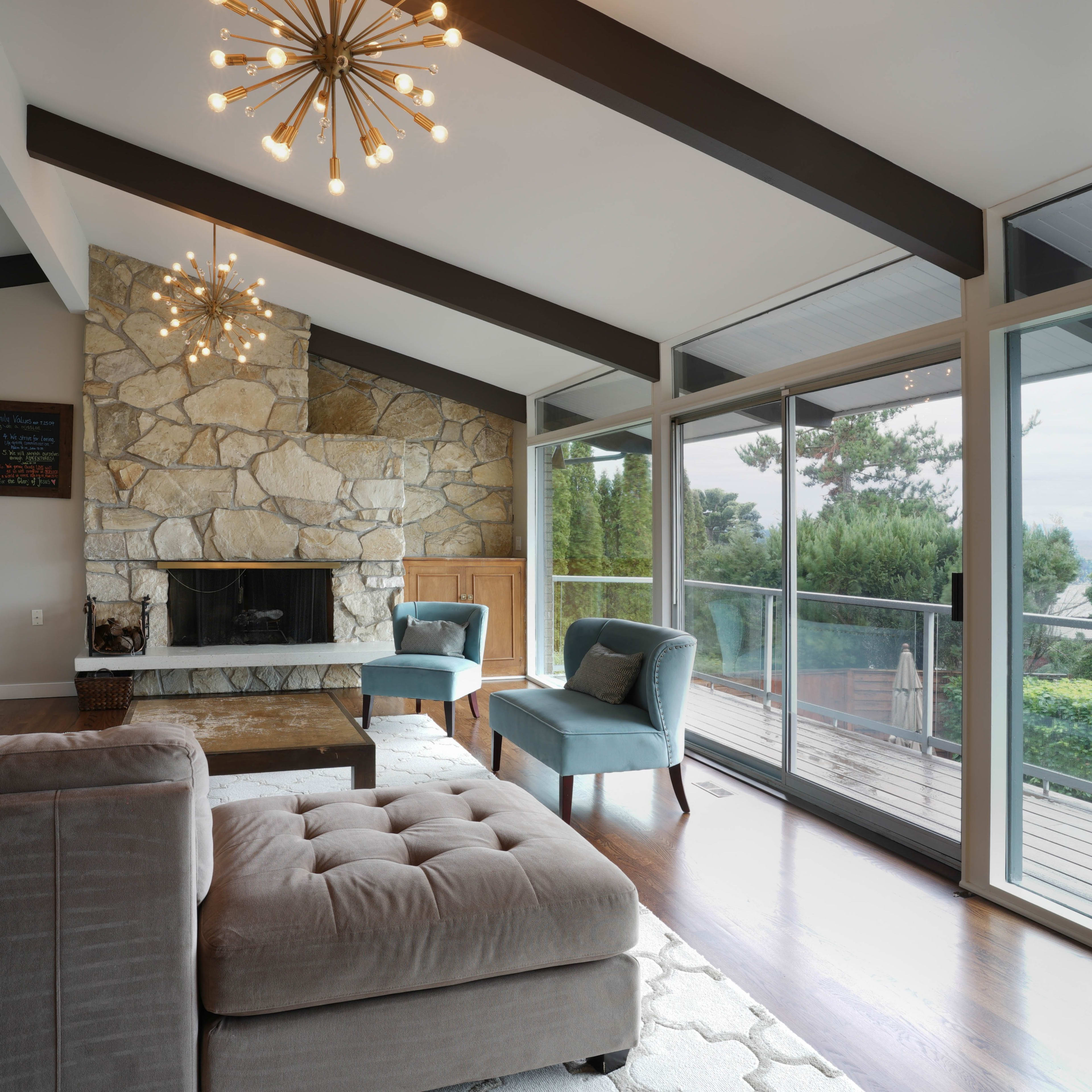 A modern living room with a stone fireplace, large windows, and contemporary lighting fixtures.