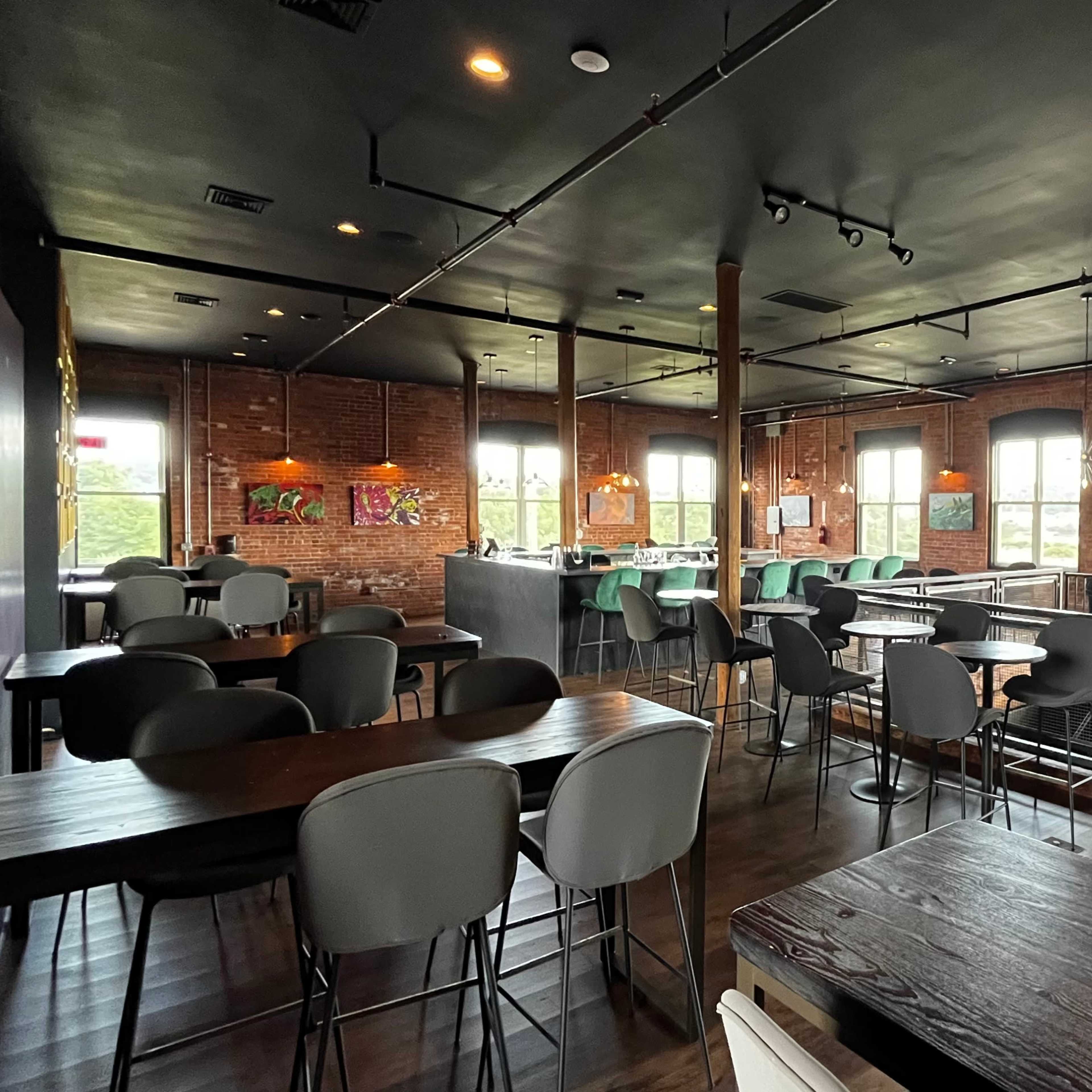 A modern, open dining area with empty tables and chairs, large windows, and colorful artwork on the walls.