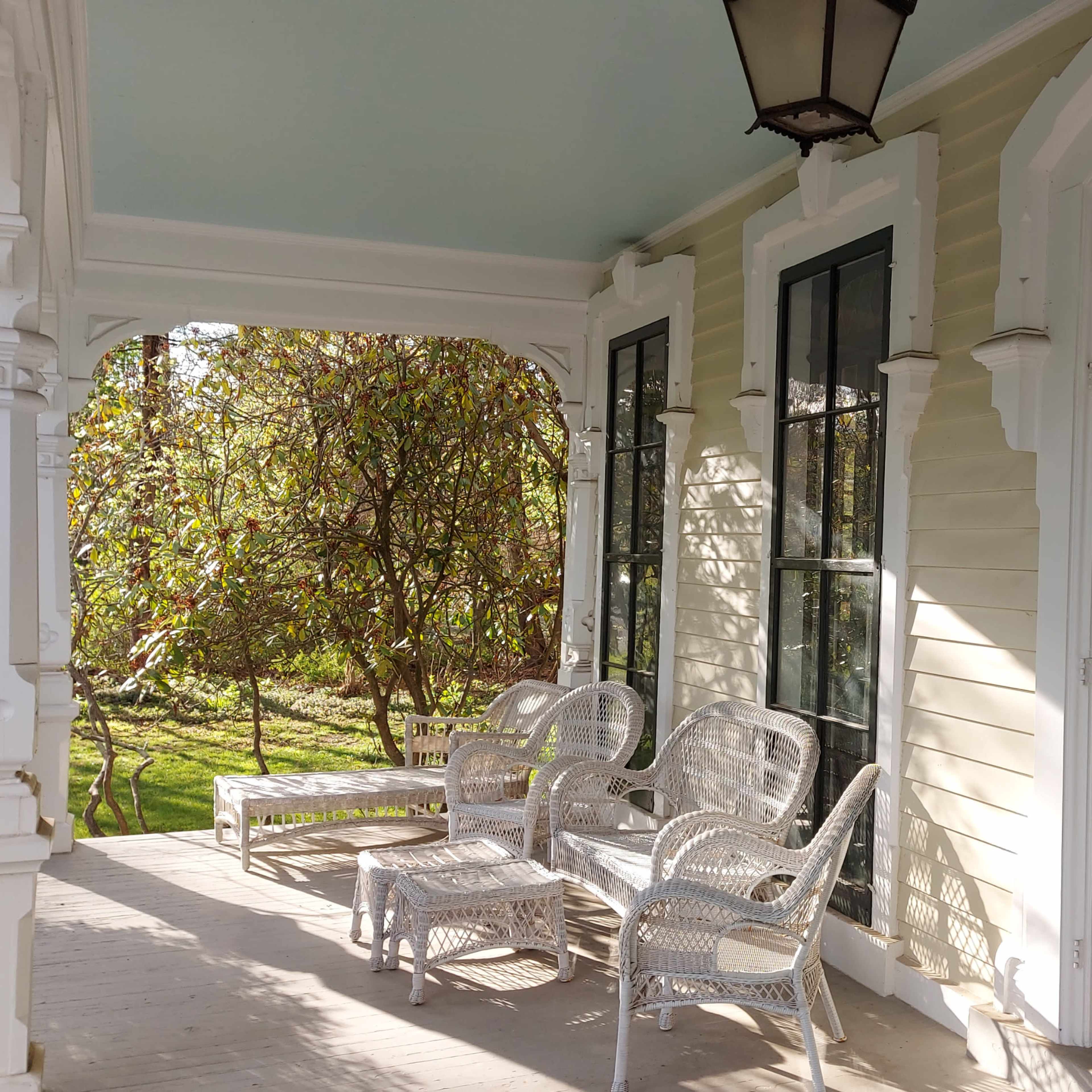 A porch with wicker chairs and a double door entrance, surrounded by greenery.