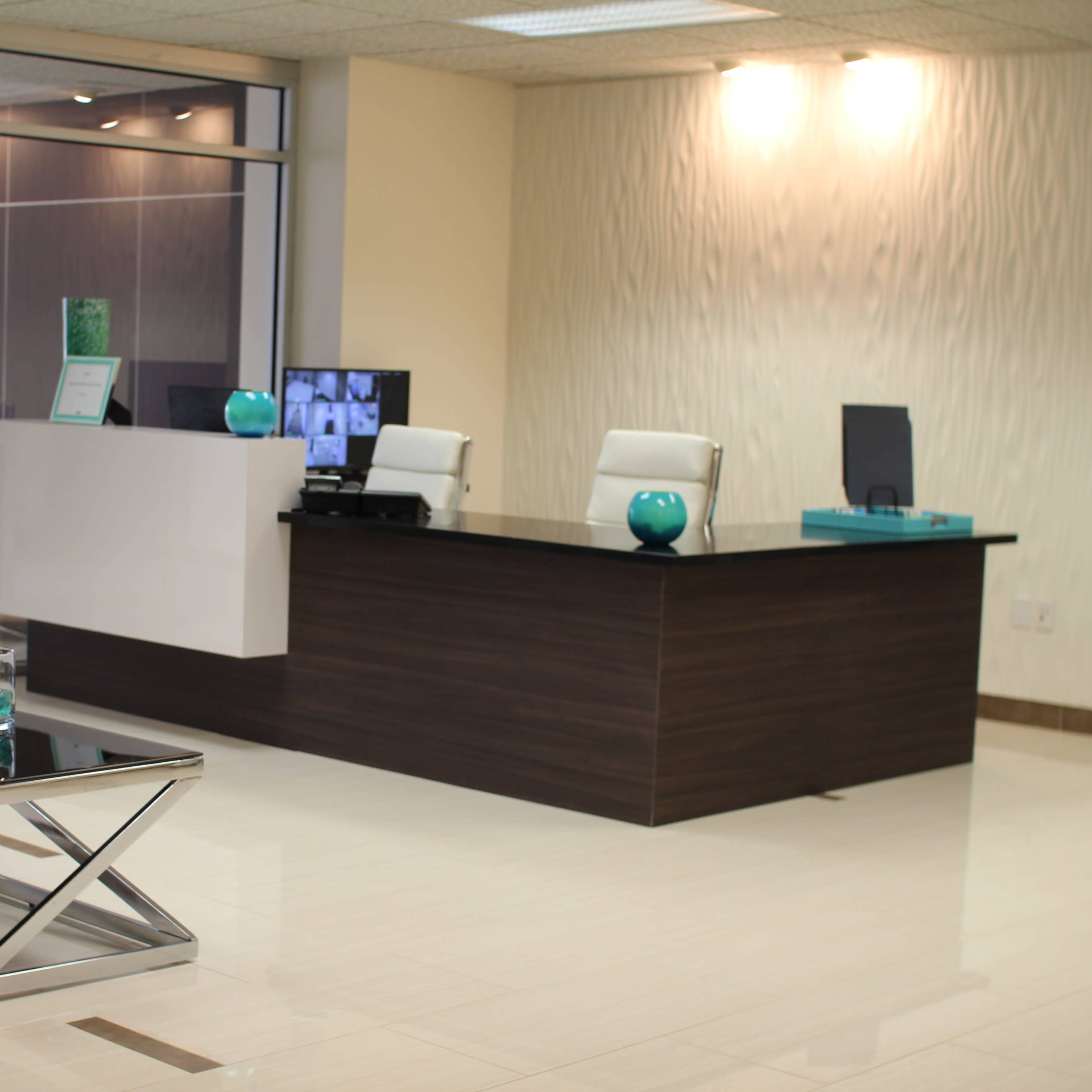 A modern reception area featuring a sleek wooden desk, two white chairs, and decorative elements like plants and turquoise accessories.