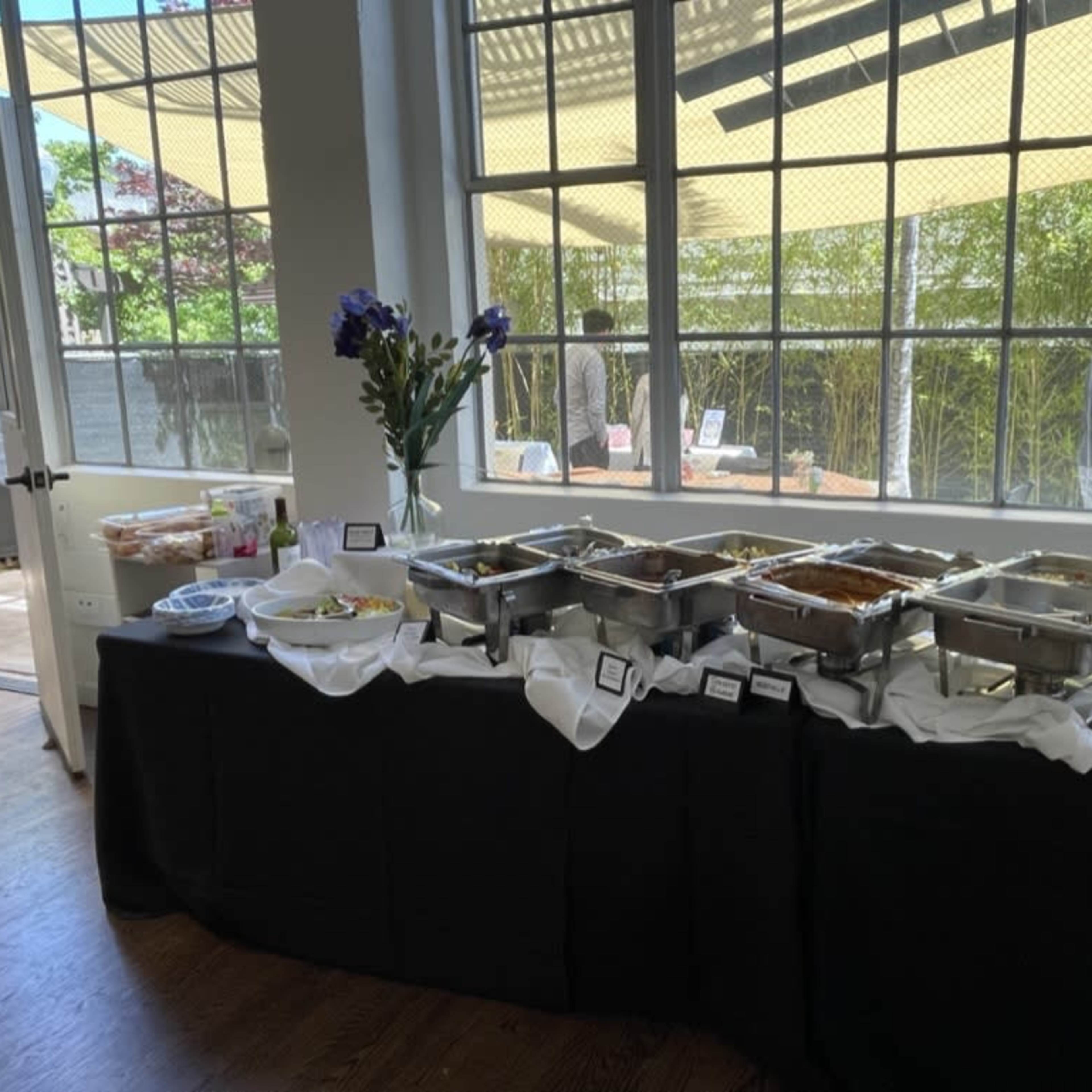 A buffet table filled with various food dishes is displayed in front of large windows.