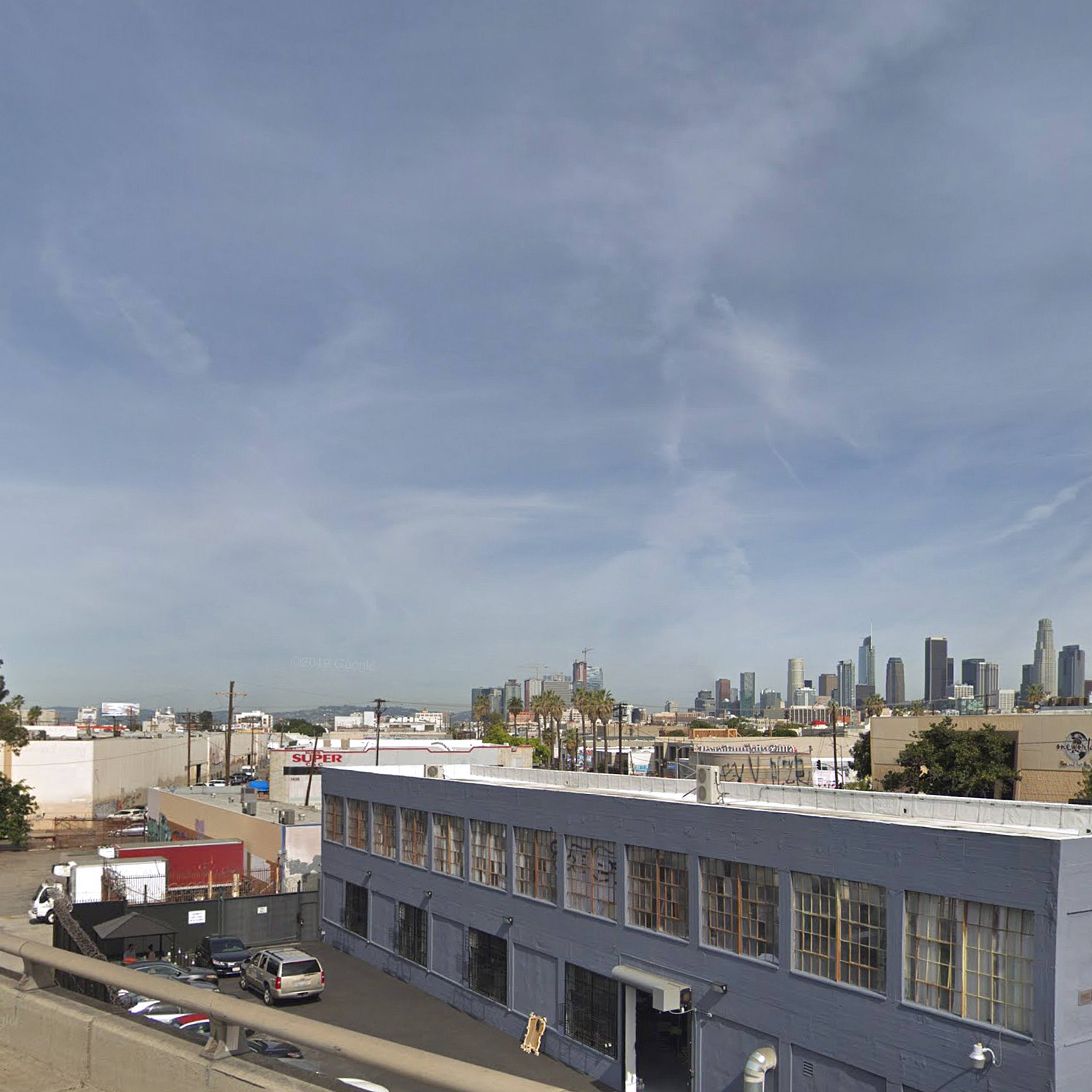 A view of downtown Los Angeles skyline from an industrial area, with a low-rise building in the foreground.