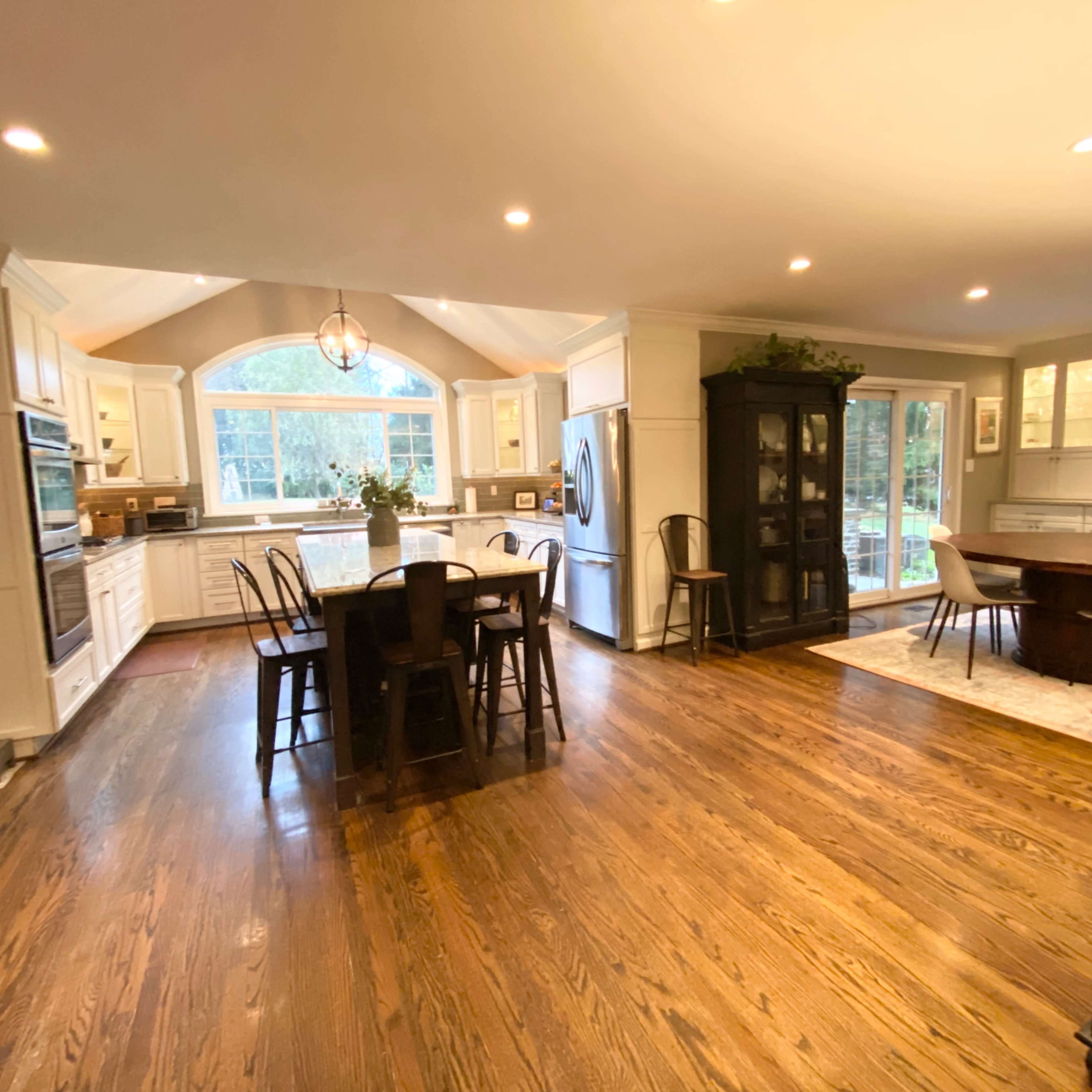 A spacious kitchen with white cabinetry, a large island with seating, and a dining area that features a glass door leading to a patio.