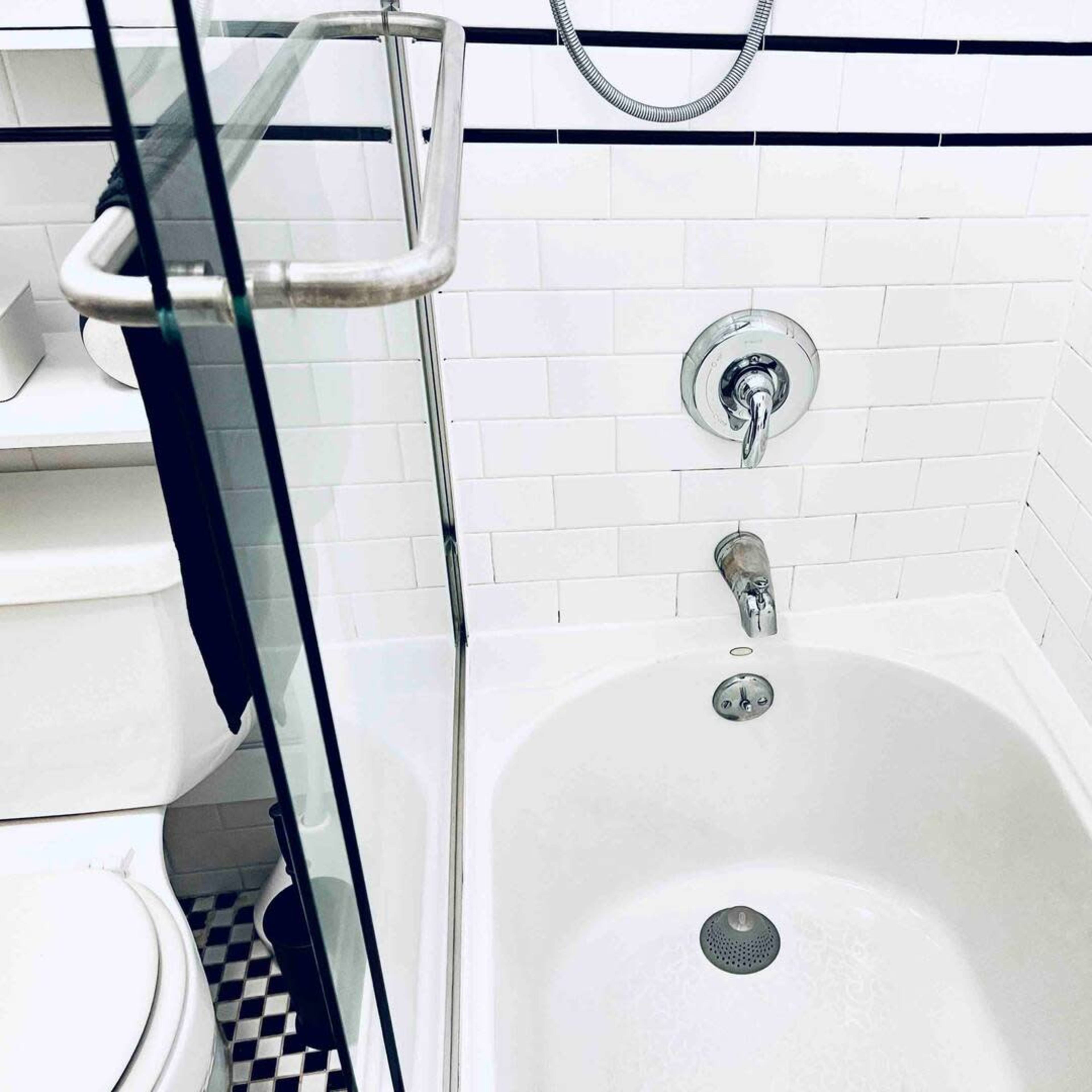 A white tiled bathroom with a shower and bathtub, featuring a glass partition and a black and white checkered floor.