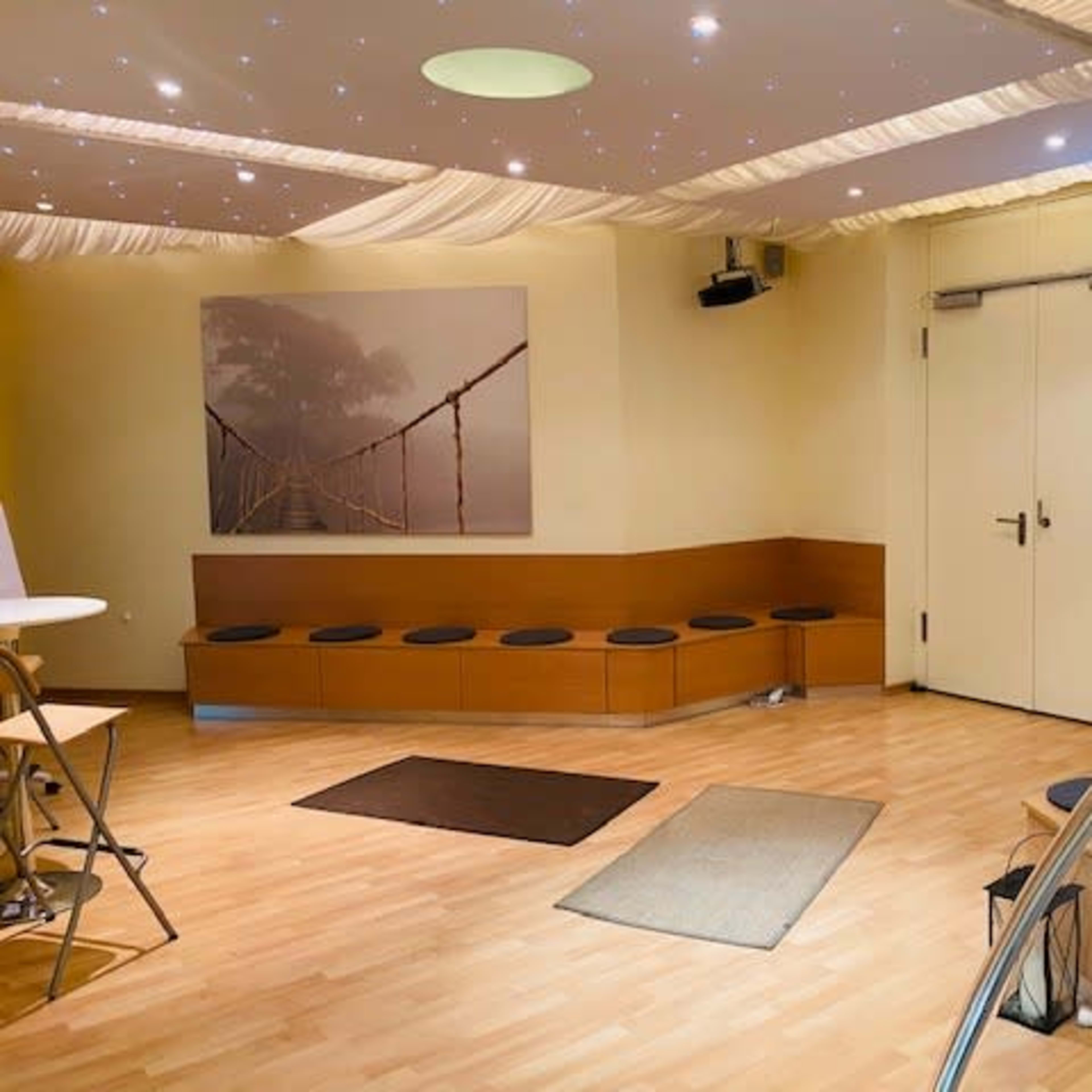A minimalistic room with a wooden bench along one wall, a table, and a soft-lit ceiling featuring star-like lights.