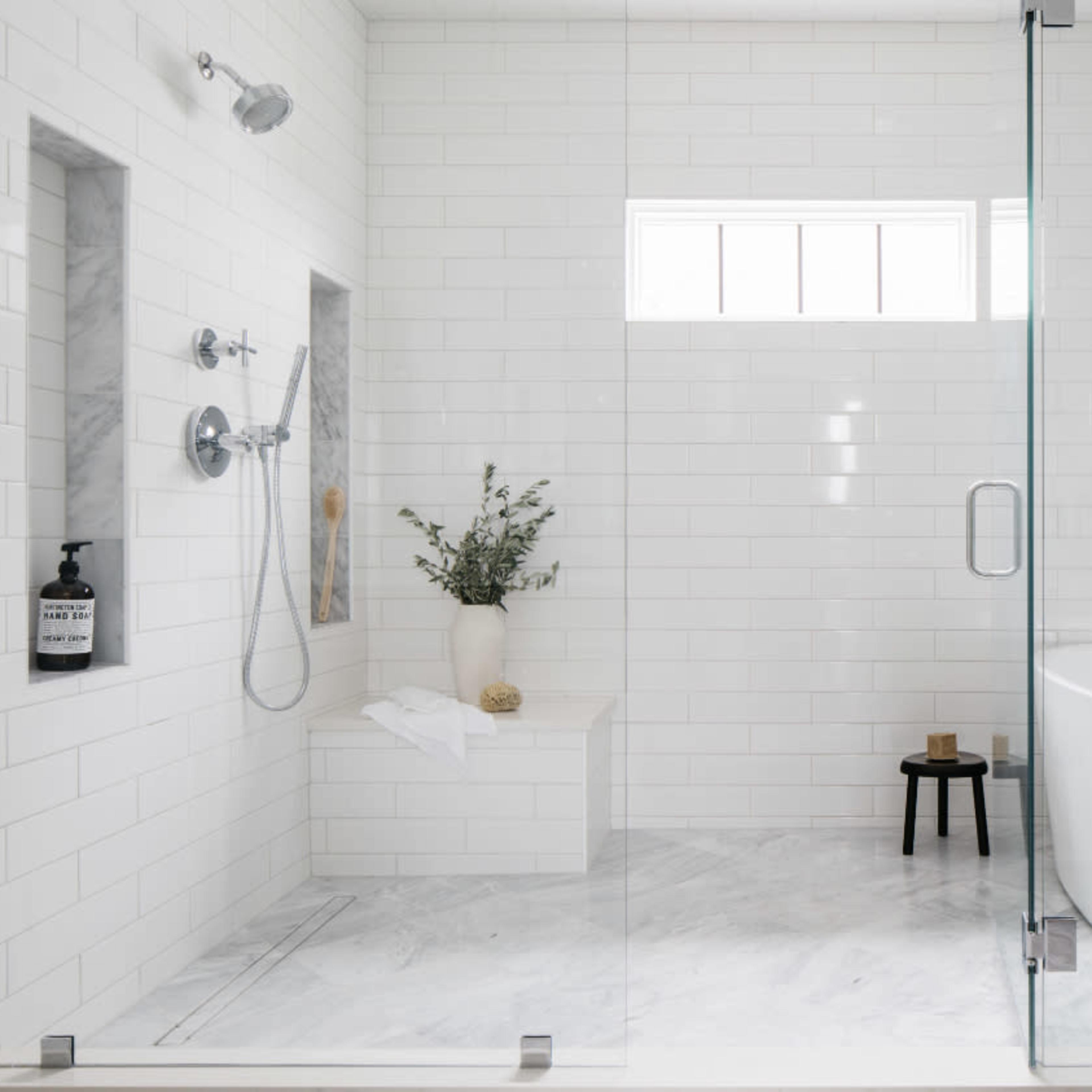 A modern, white-tiled bathroom with a glass shower enclosure and a freestanding bathtub.