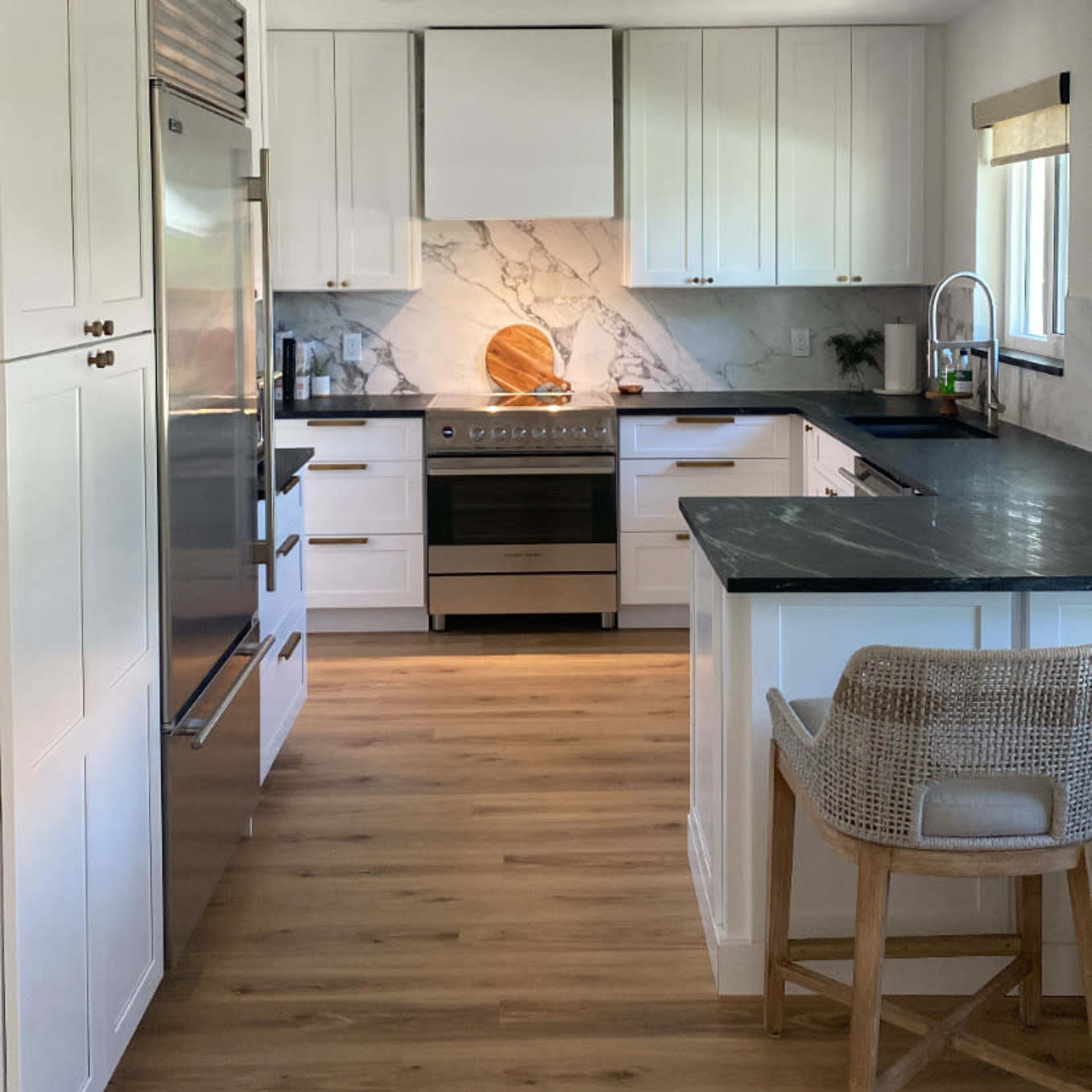 A modern kitchen features white cabinetry, a marble backsplash with a circular wooden accent, stainless steel appliances, and wooden flooring.