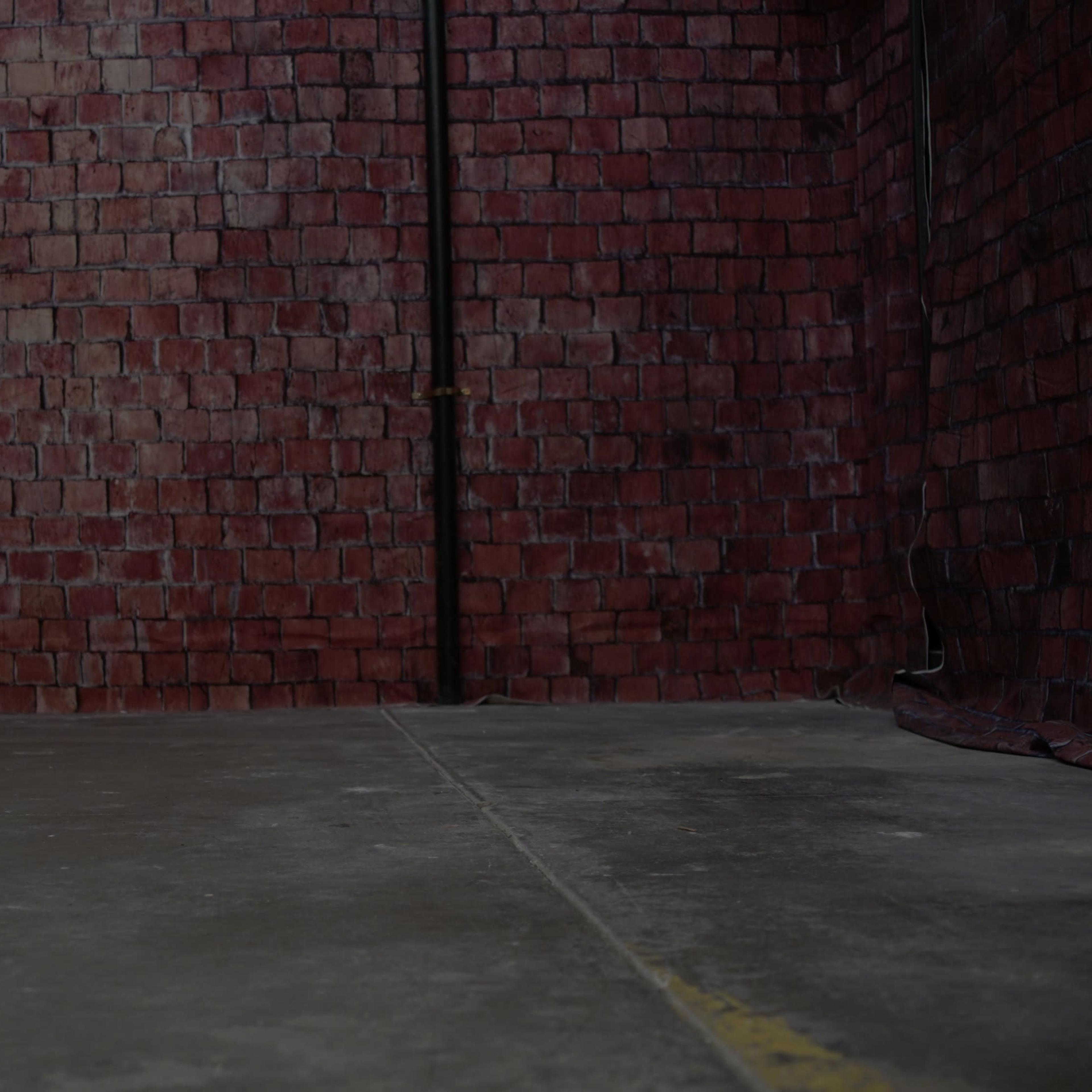 An empty interior space with a concrete floor and a red brick wall in the background.
