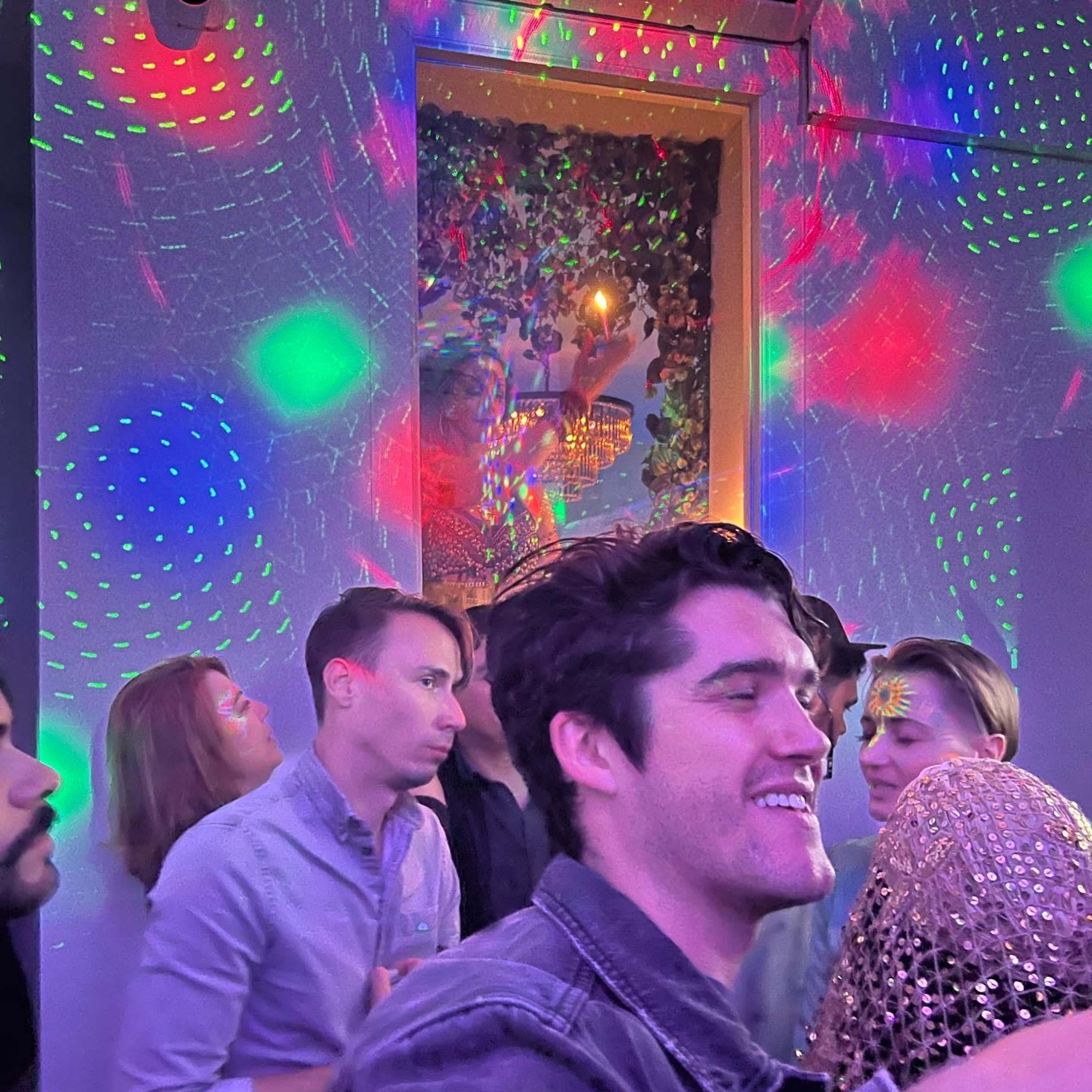 A group of people are dancing in a dimly lit room with colorful lights projecting onto the walls.