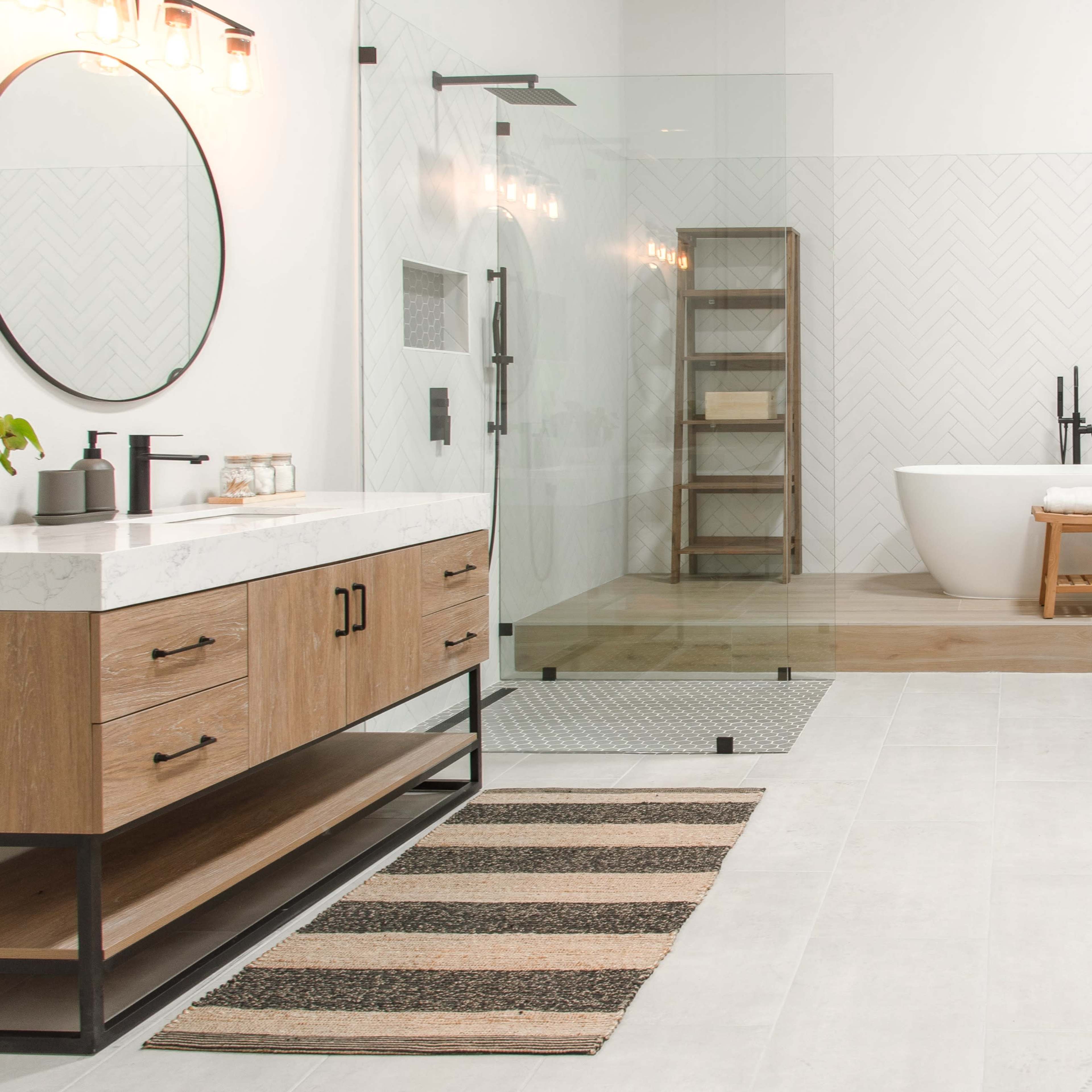 A modern bathroom featuring a freestanding bathtub, a glass-enclosed shower, a wooden vanity with a marble countertop, and a striped area rug.
