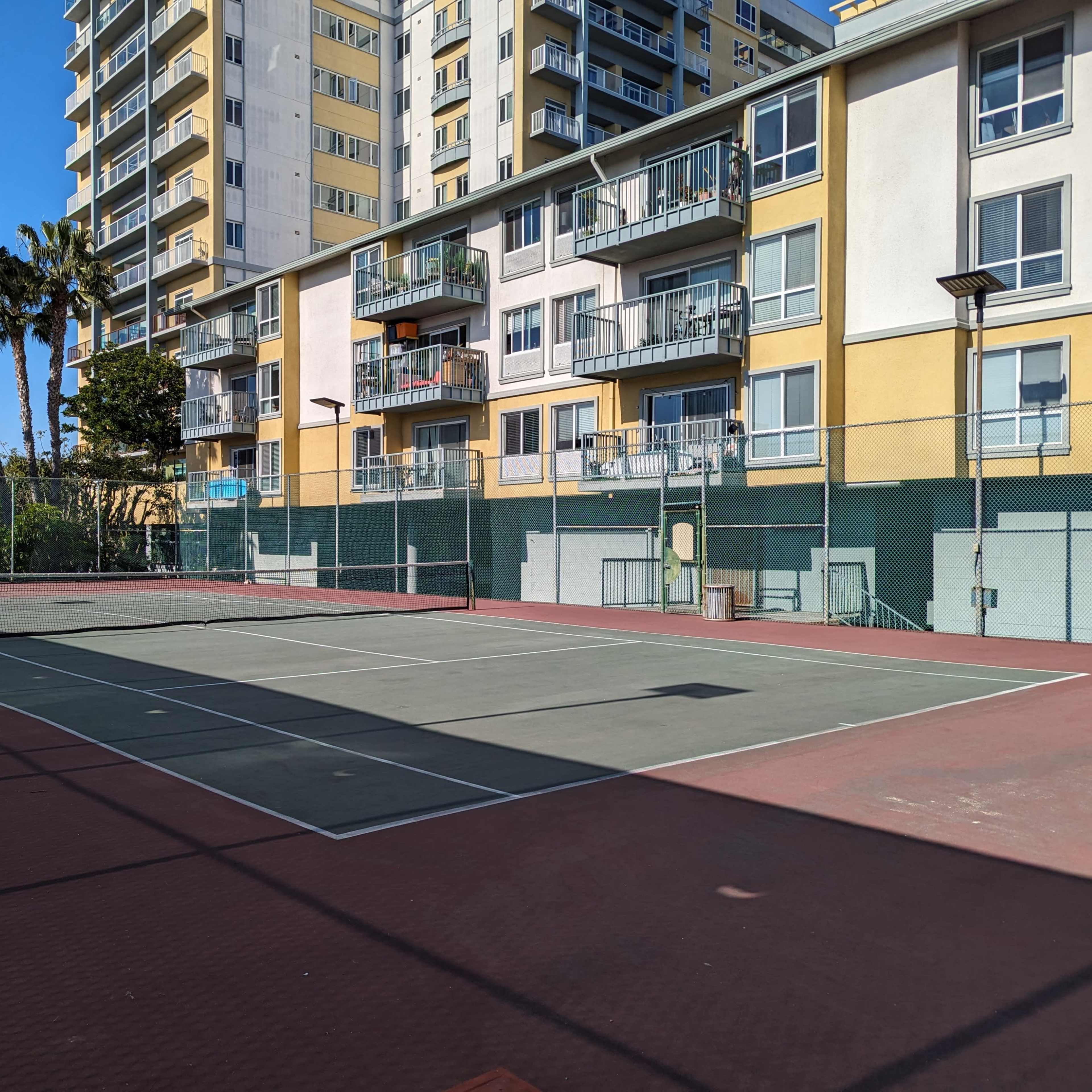 A tennis court surrounded by palm trees and a multi-story residential building.