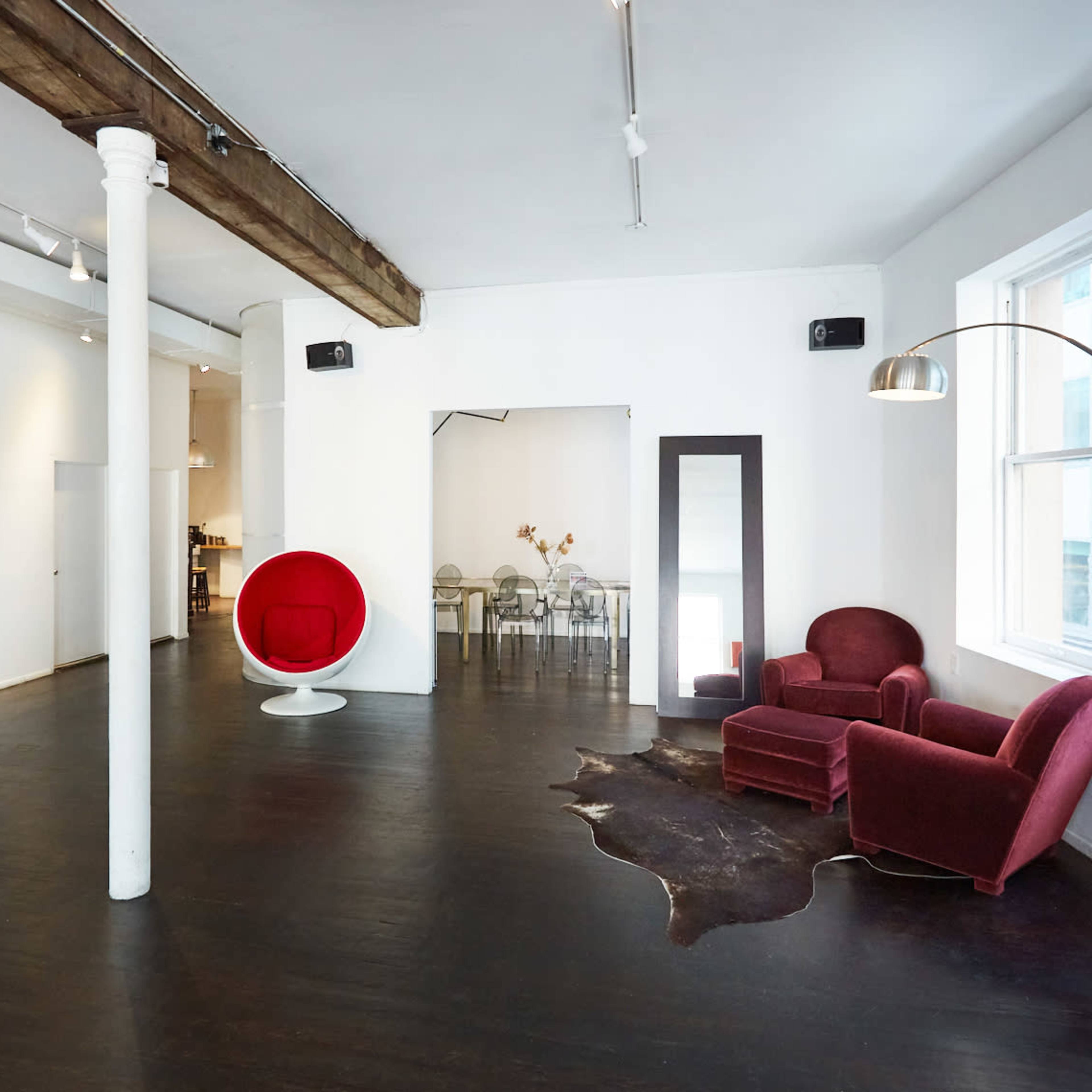 A spacious room features a red chair, a white pod chair, a large mirror, and a wooden beam across the ceiling.
