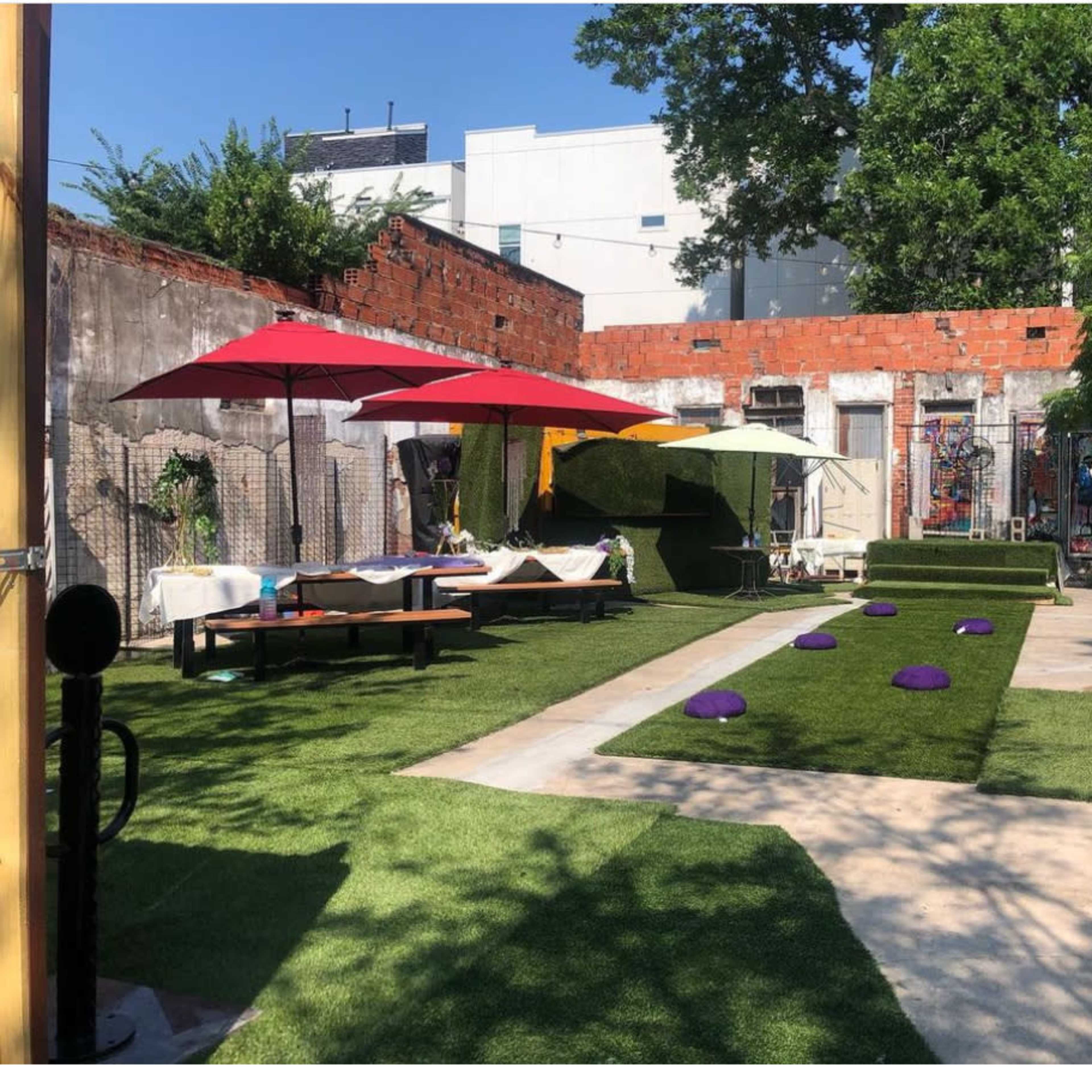 An outdoor space with artificial grass, various seating areas, and colorful umbrellas providing shade.