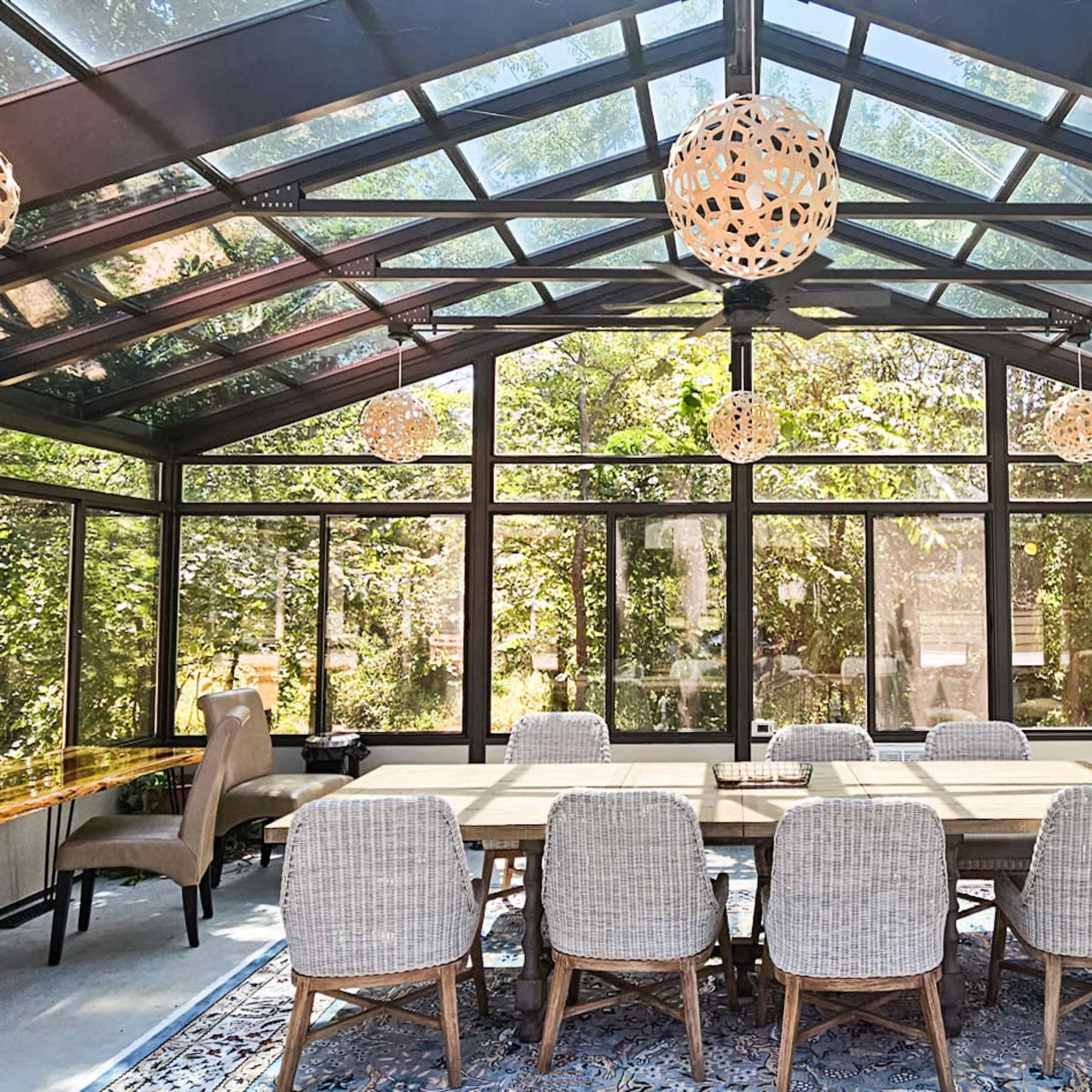 A spacious sunroom with large glass windows, a dining table, and several decorative light fixtures.