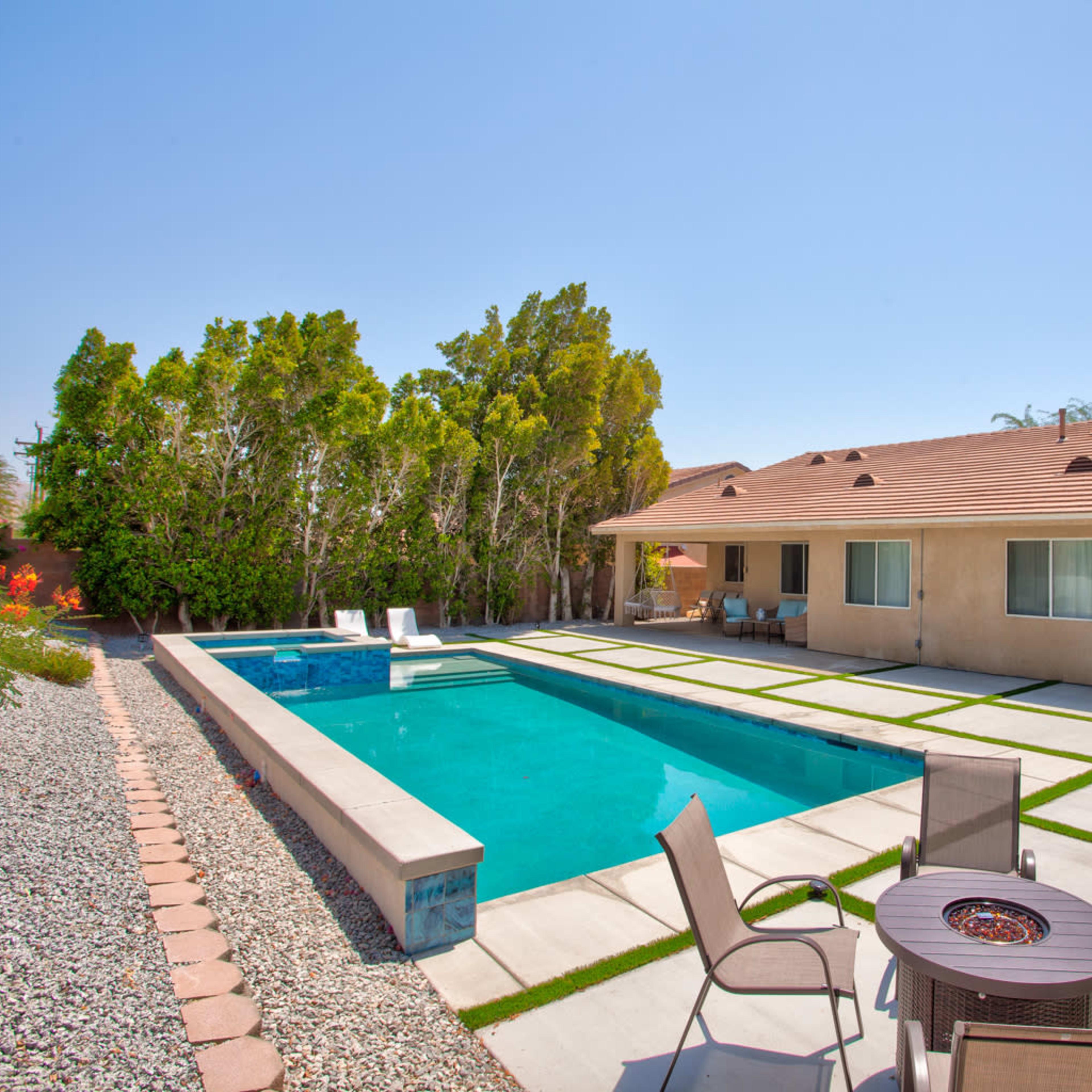 A backyard with a swimming pool, lounge chairs, and a fire pit surrounded by landscaped gravel and grass.