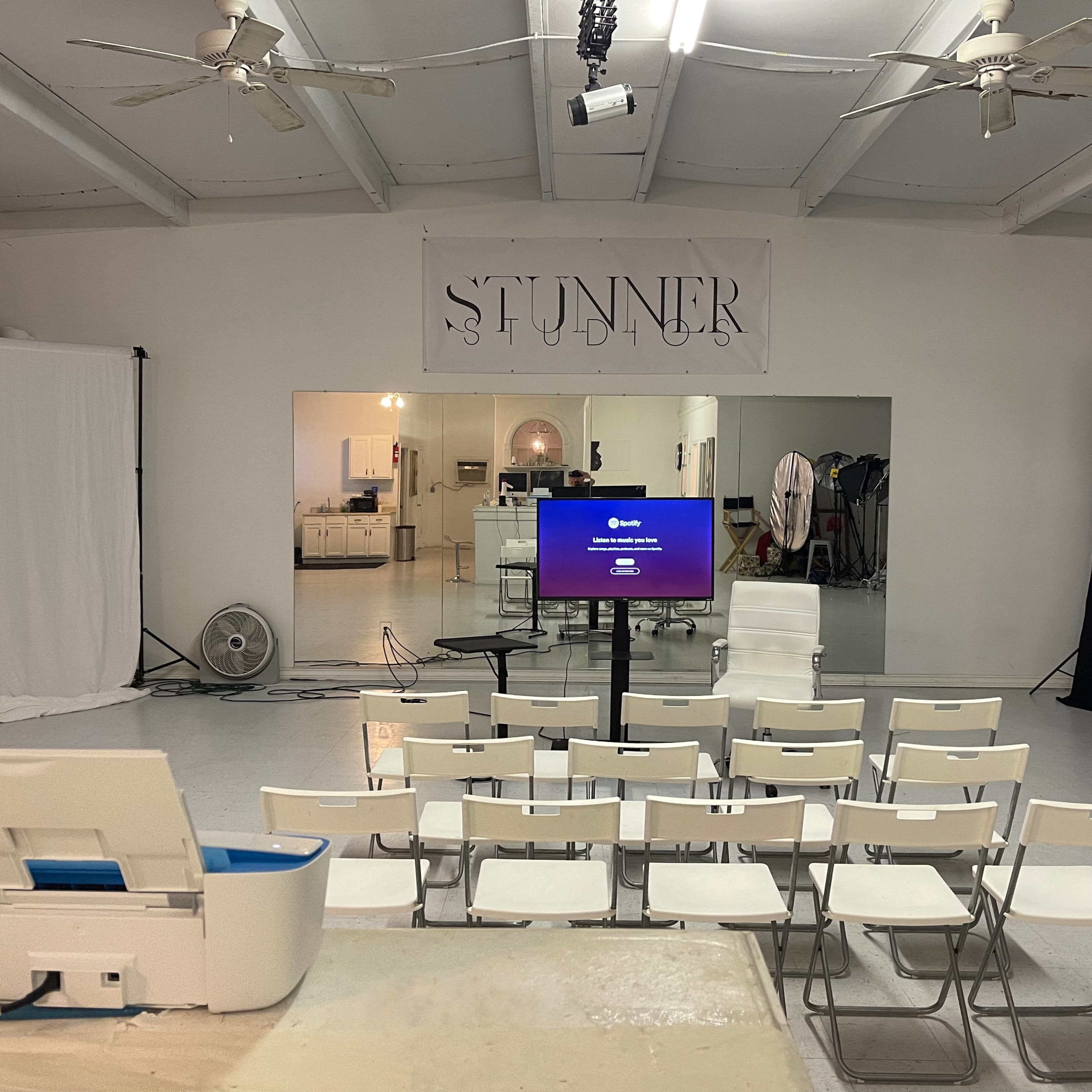 A minimalist studio setup with rows of chairs facing a screen, framed by white walls and a large banner stating "STUNNER."