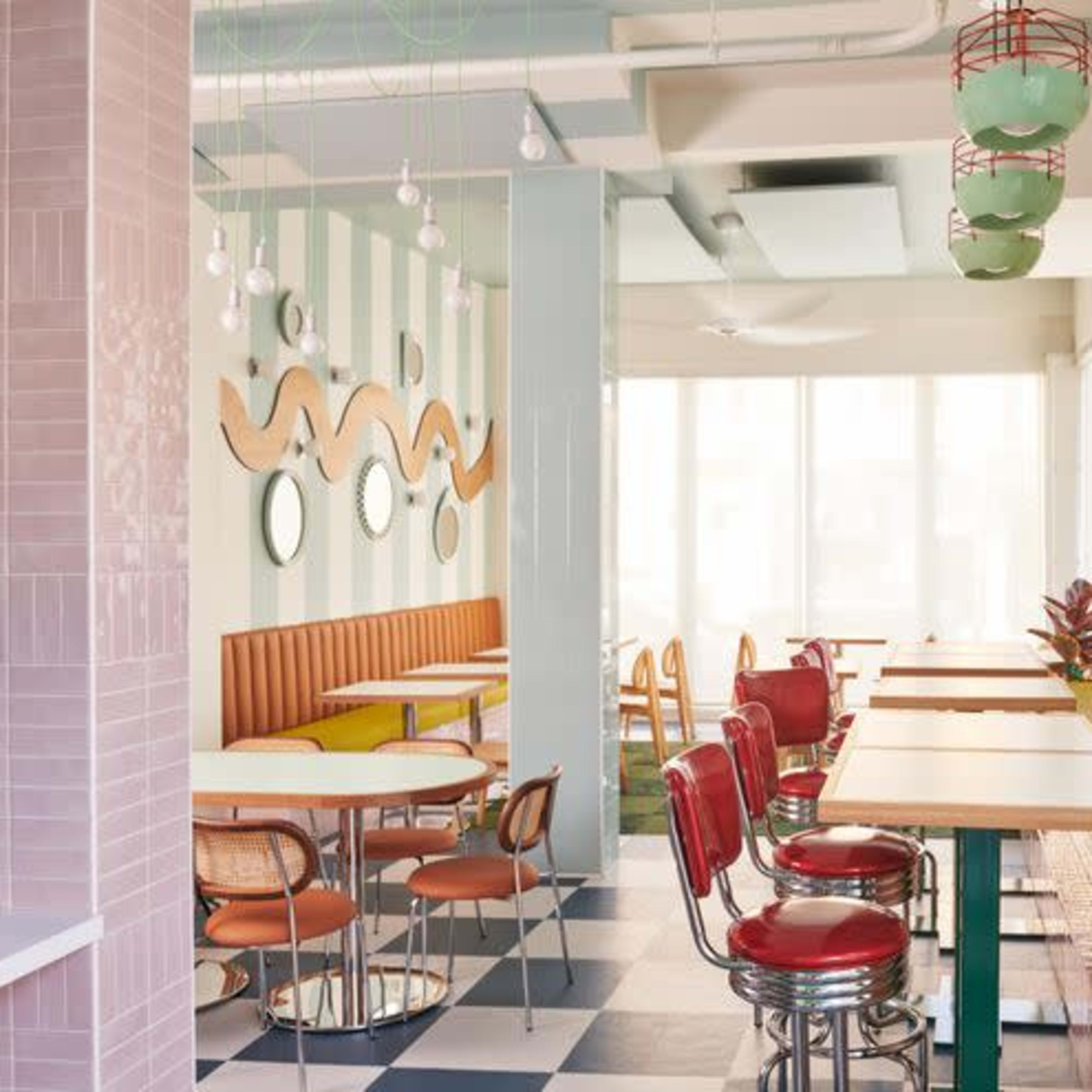 A vibrant café interior featuring striped walls, a combination of circular and square tables, and cushioned seating against a backdrop of large windows.