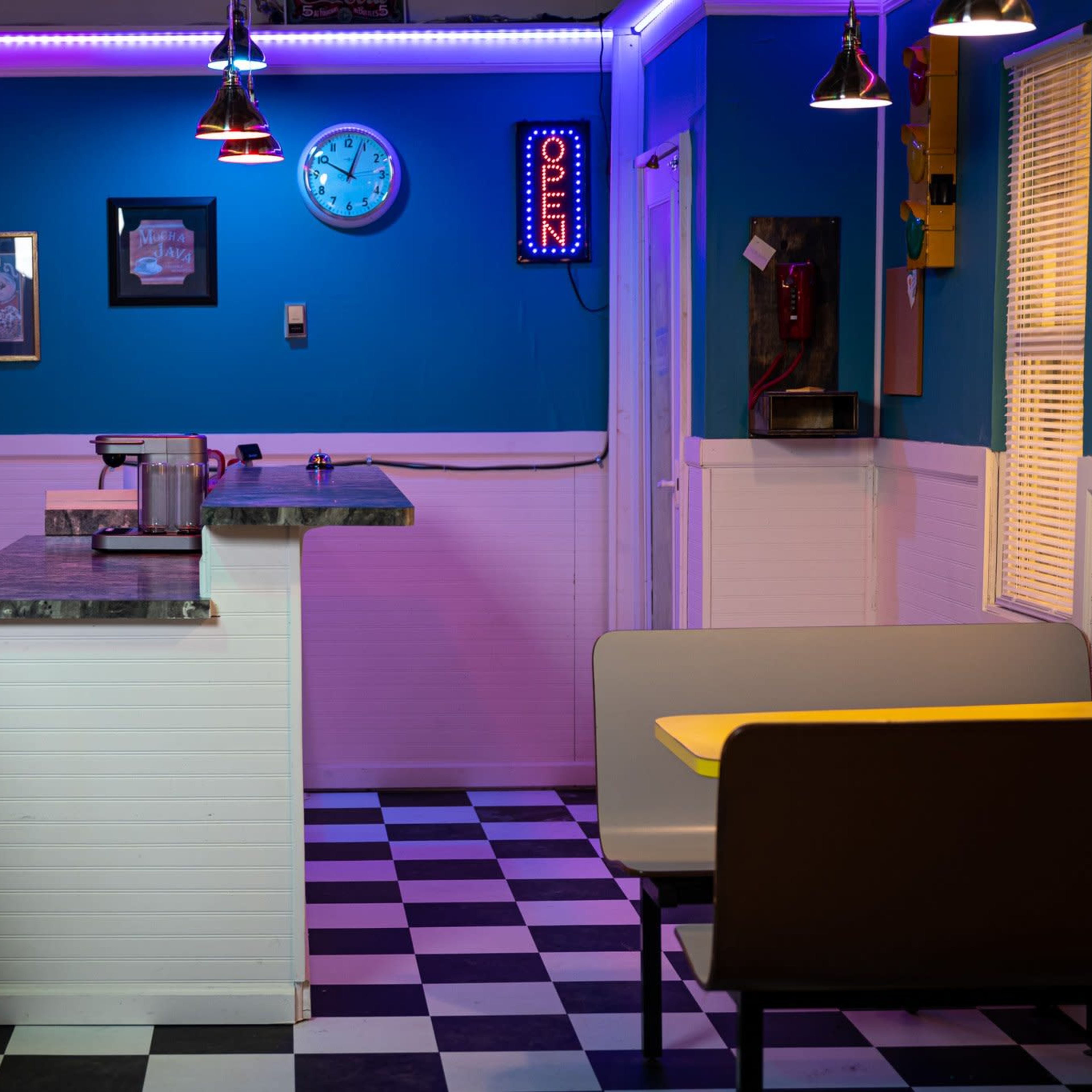 A retro diner interior with a checkered floor, a countertop, a vintage jukebox, and neon lighting.