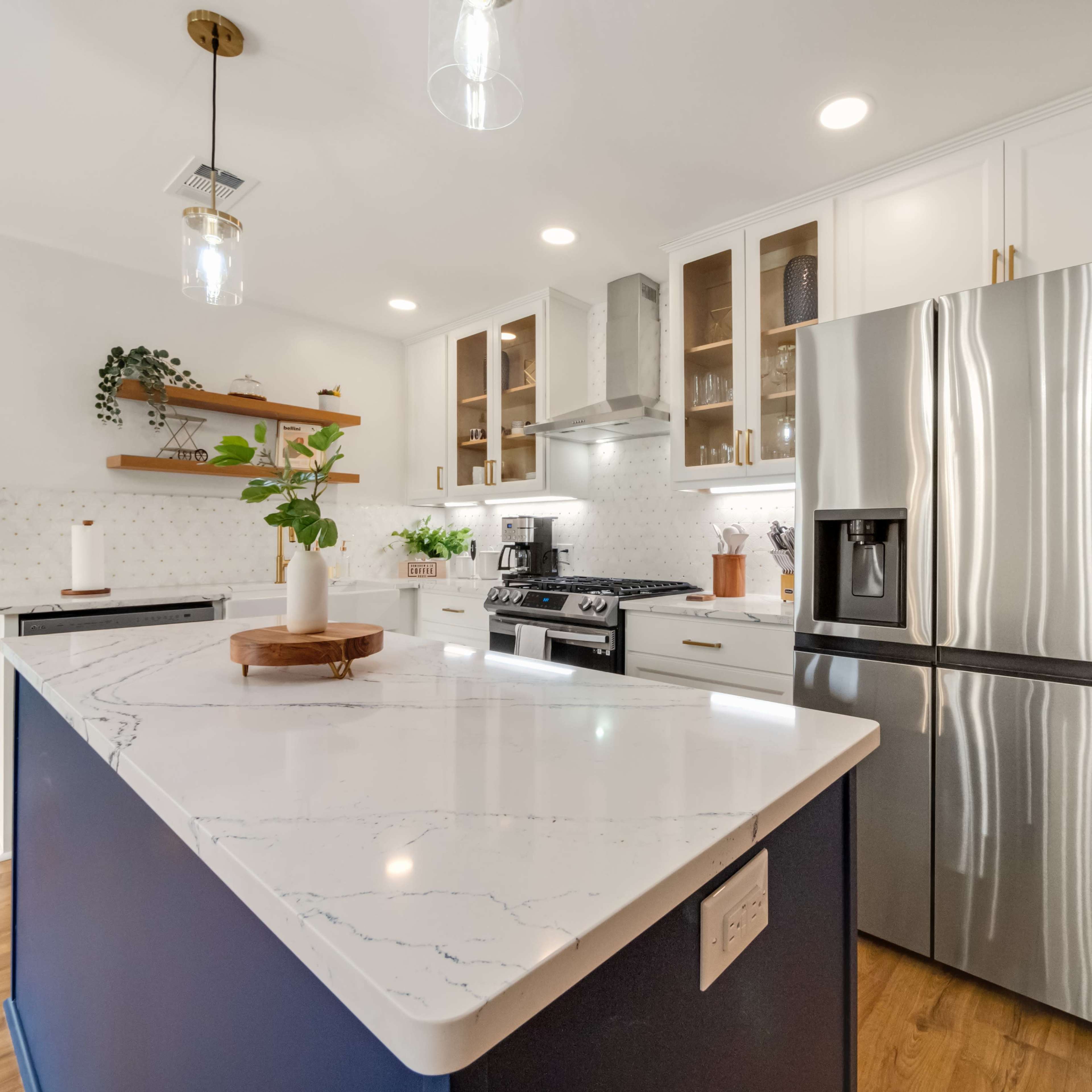 A modern kitchen featuring a large island with a marble countertop, stainless steel appliances, and white cabinetry.