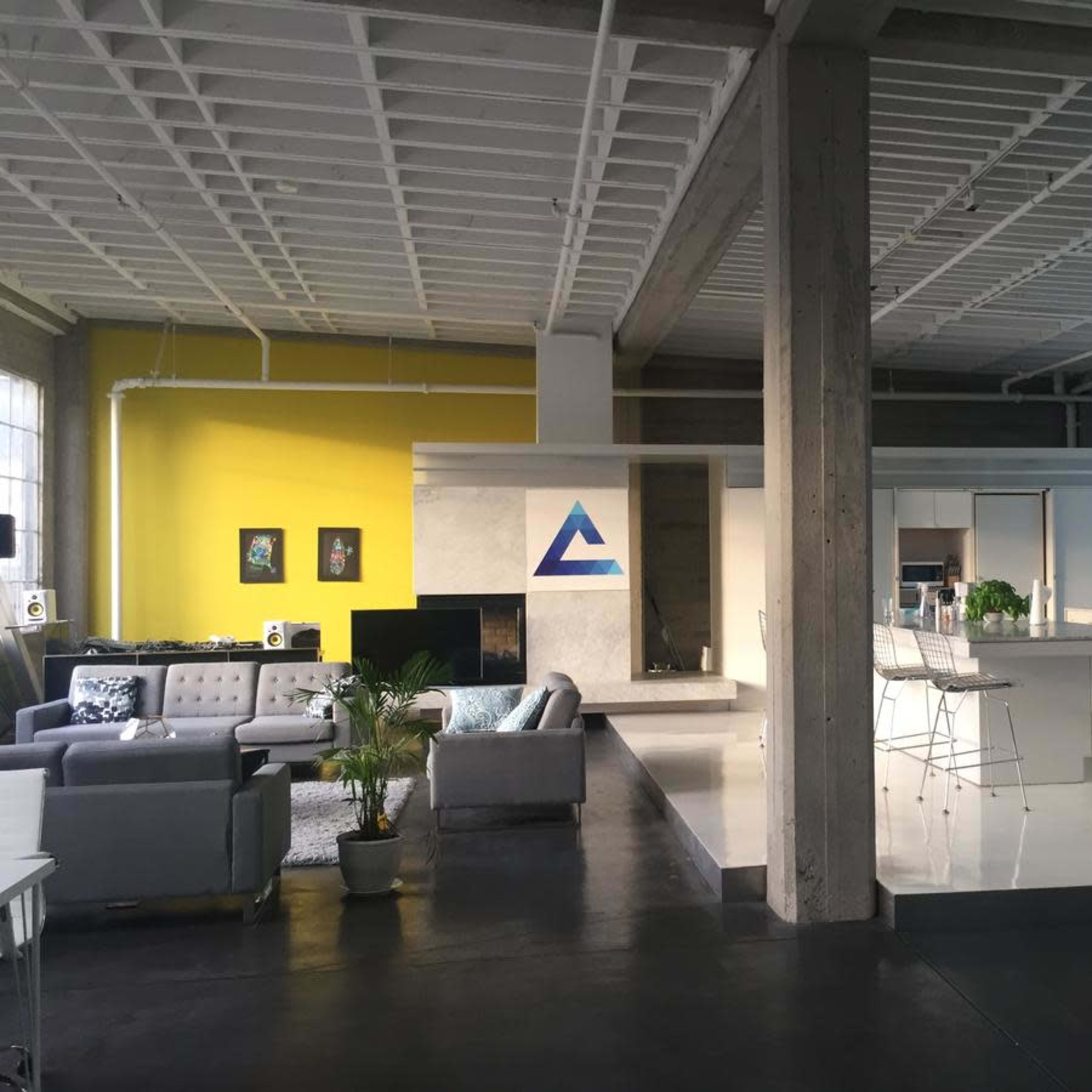 A modern, open-concept living area and kitchen with a mix of gray and yellow walls, concrete pillars, and sleek white furniture.