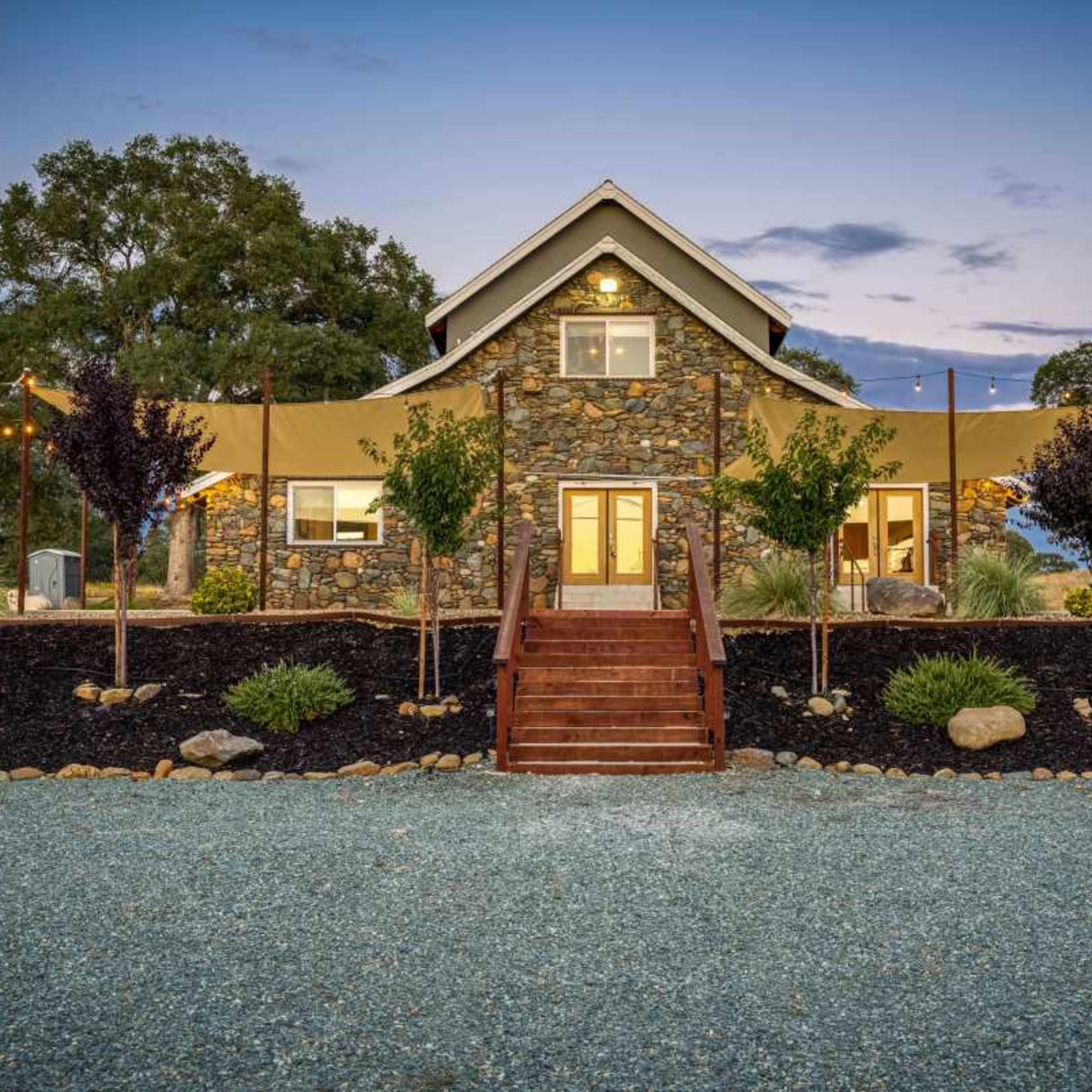 A stone house with a sloped roof, surrounded by landscaped gardens and decorative lighting.